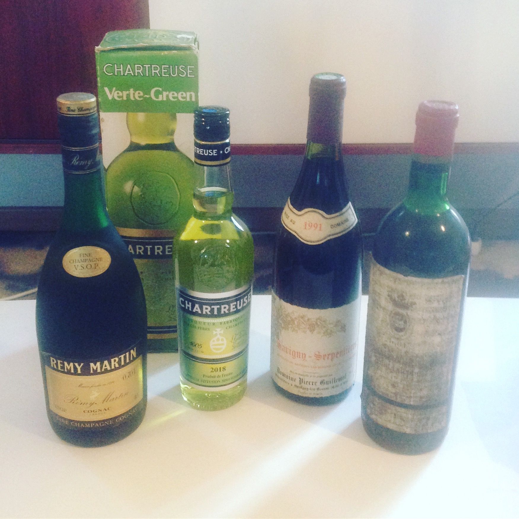 Cinq bouteilles d'alcool sur une table. On y trouve notamment du Rémy Martin, de la Chartreuse et des bouteilles de vin.
