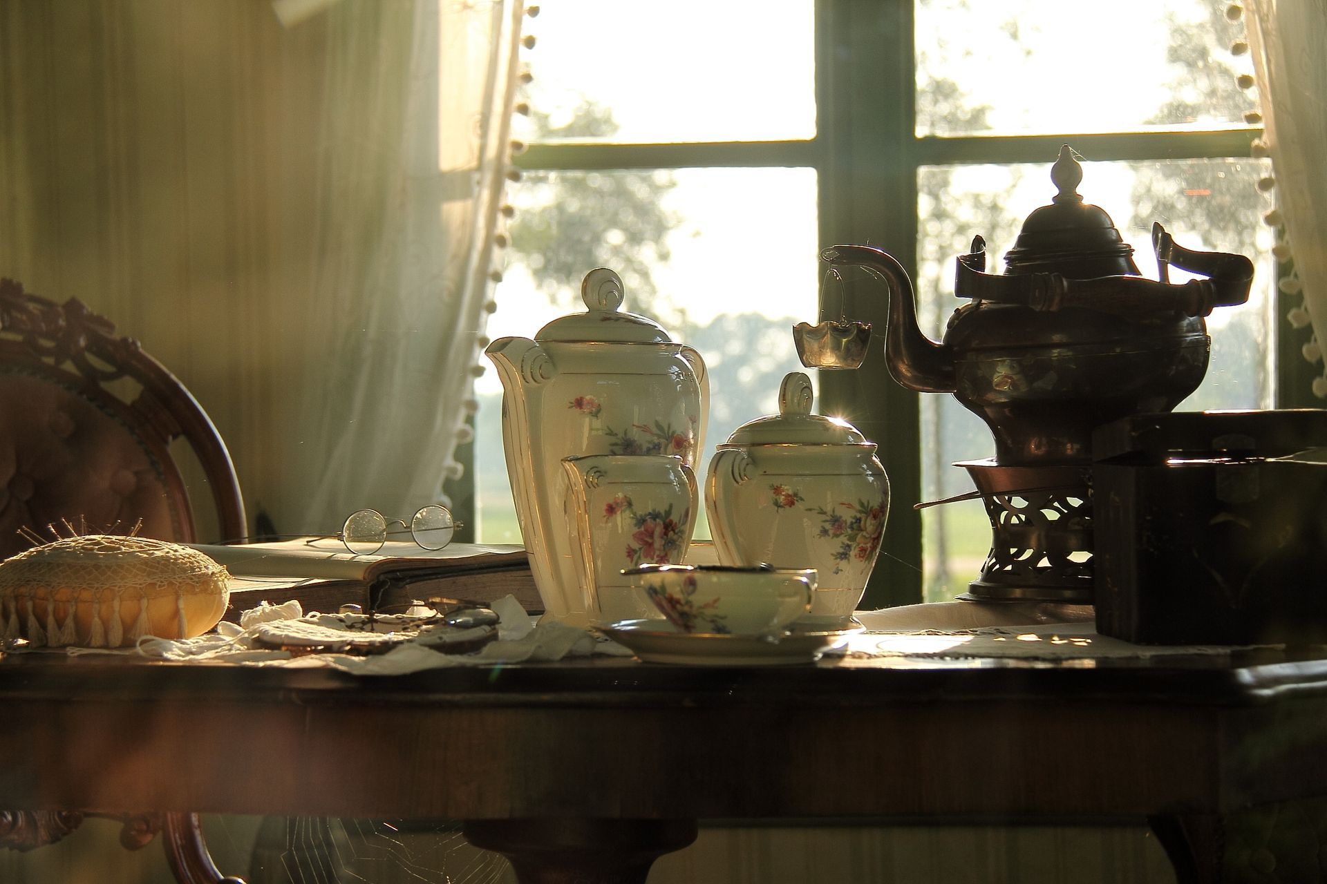 Service à thé sur une table éclairée par la lumière du soleil entrant par une fenêtre. Comprend une théière, des tasses et une brosse.