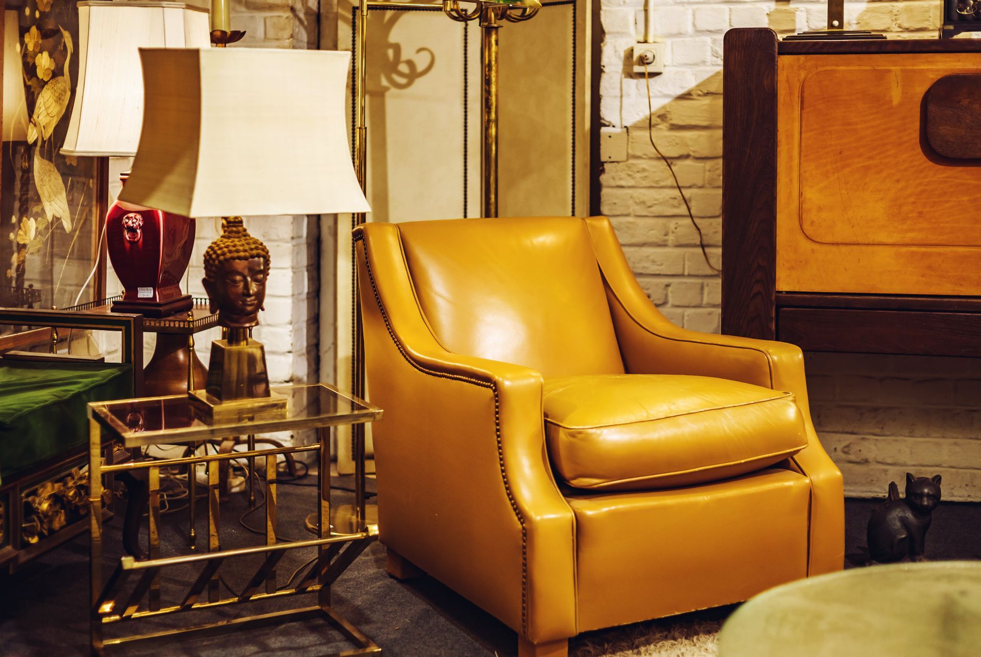 Fauteuil en cuir jaune dans une pièce de style vintage, à côté d'une table d'appoint en laiton avec une lampe.