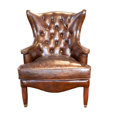 Fauteuil à oreilles capitonné en cuir marron avec pieds en bois, sur fond blanc.