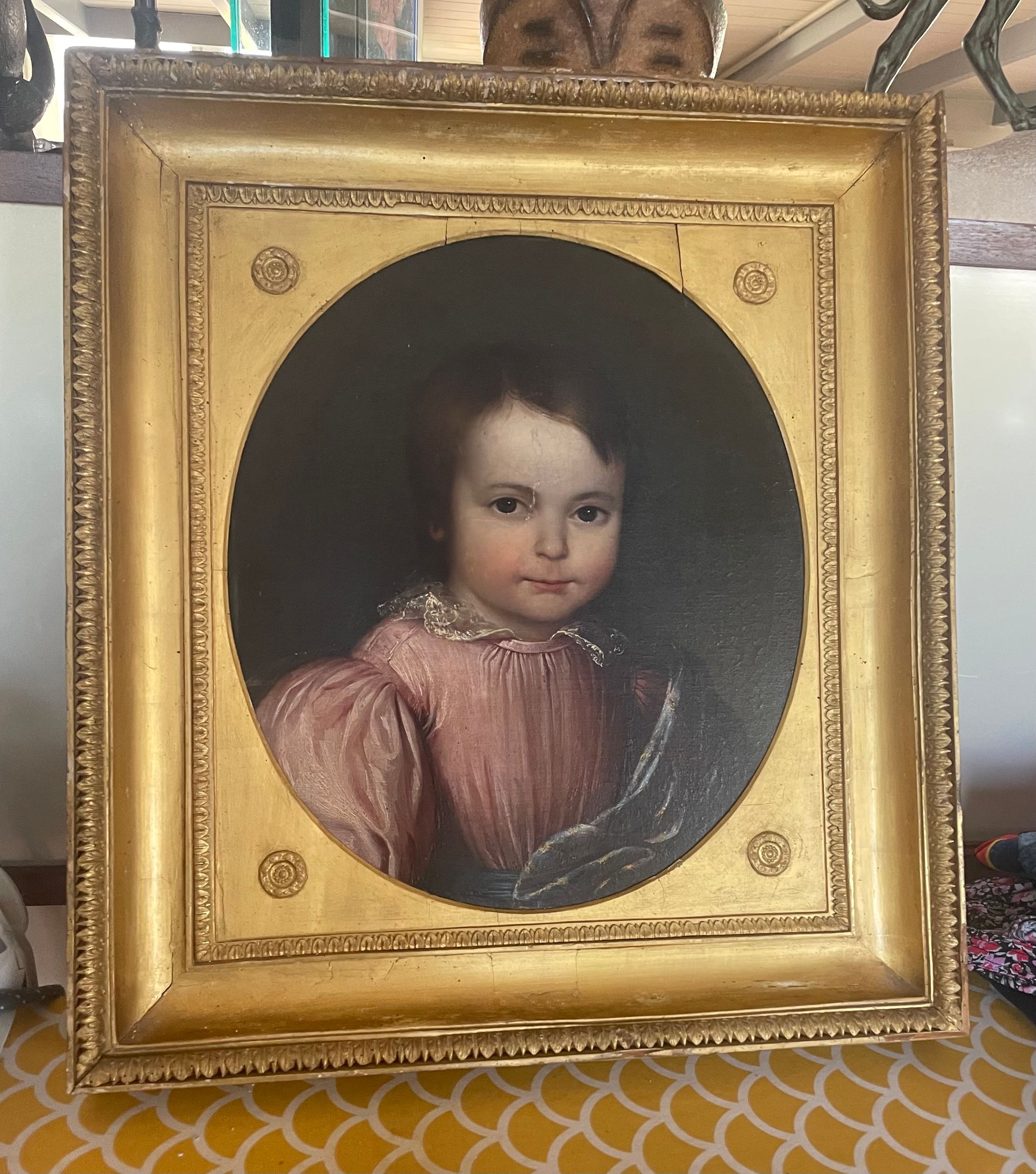 Portrait à l'huile d'une enfant en robe rose, dans un cadre doré orné.