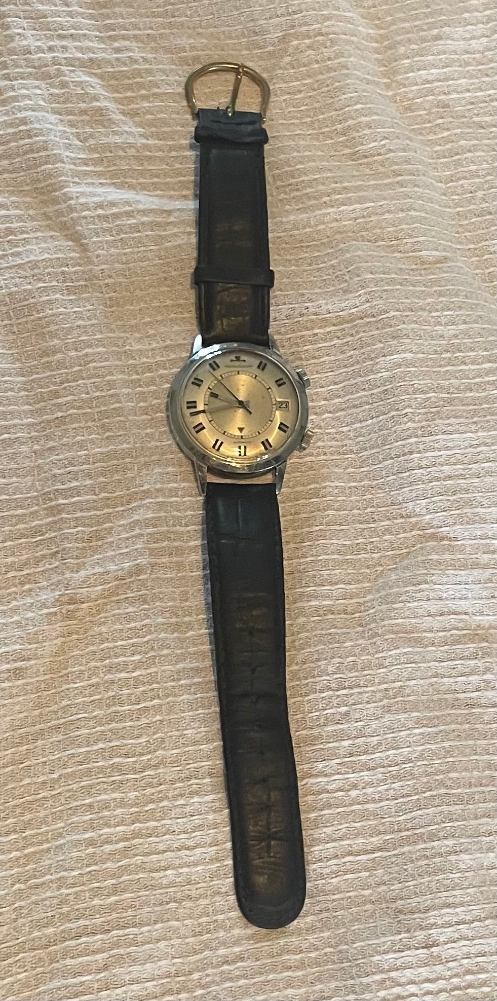 Une montre-bracelet avec un bracelet en cuir noir sur un cadran en tissu marron clair.