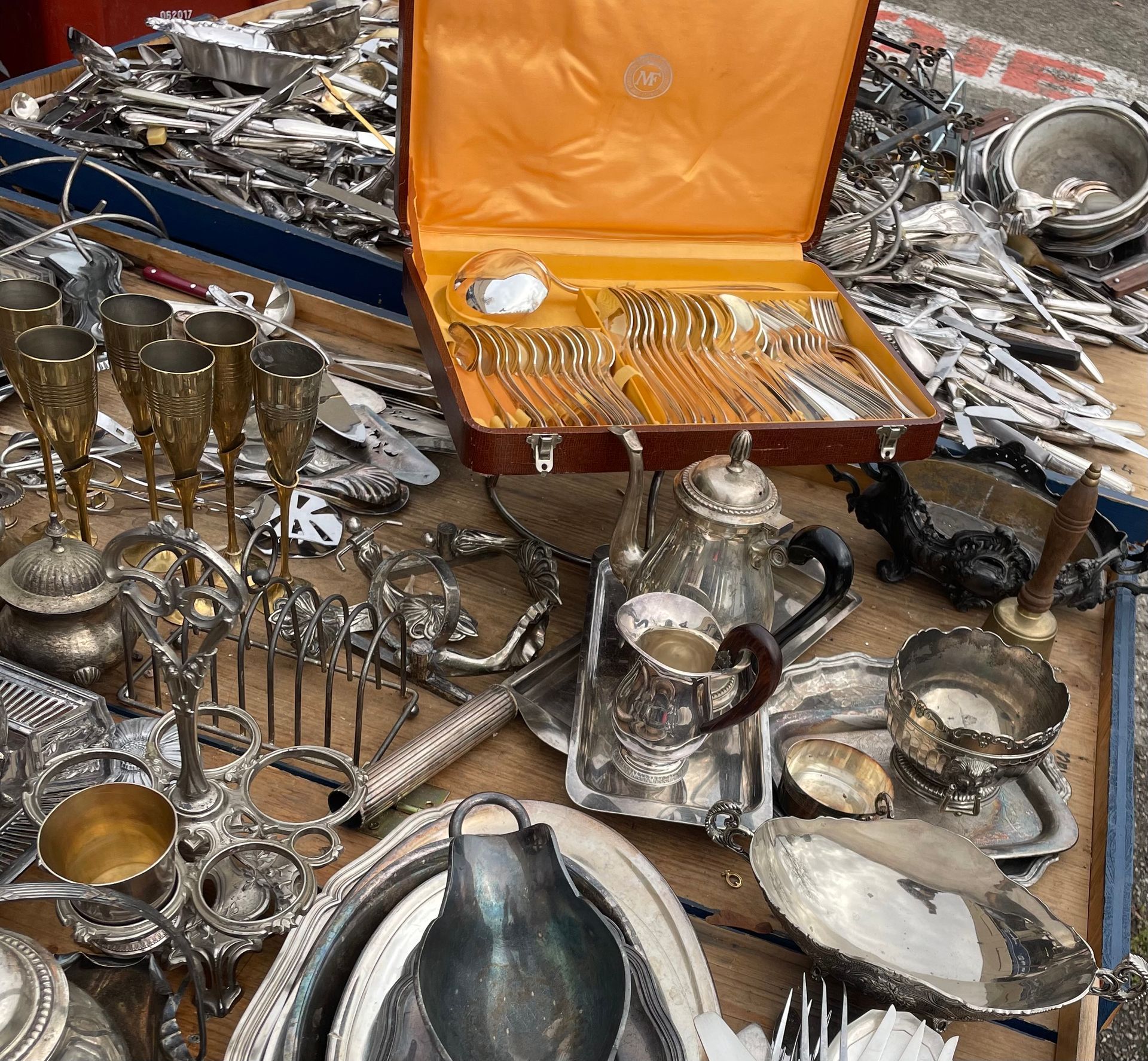 Argenterie et autres objets en métal présentés sur une table. On y trouve notamment des flûtes à champagne, un service à thé et des couverts.