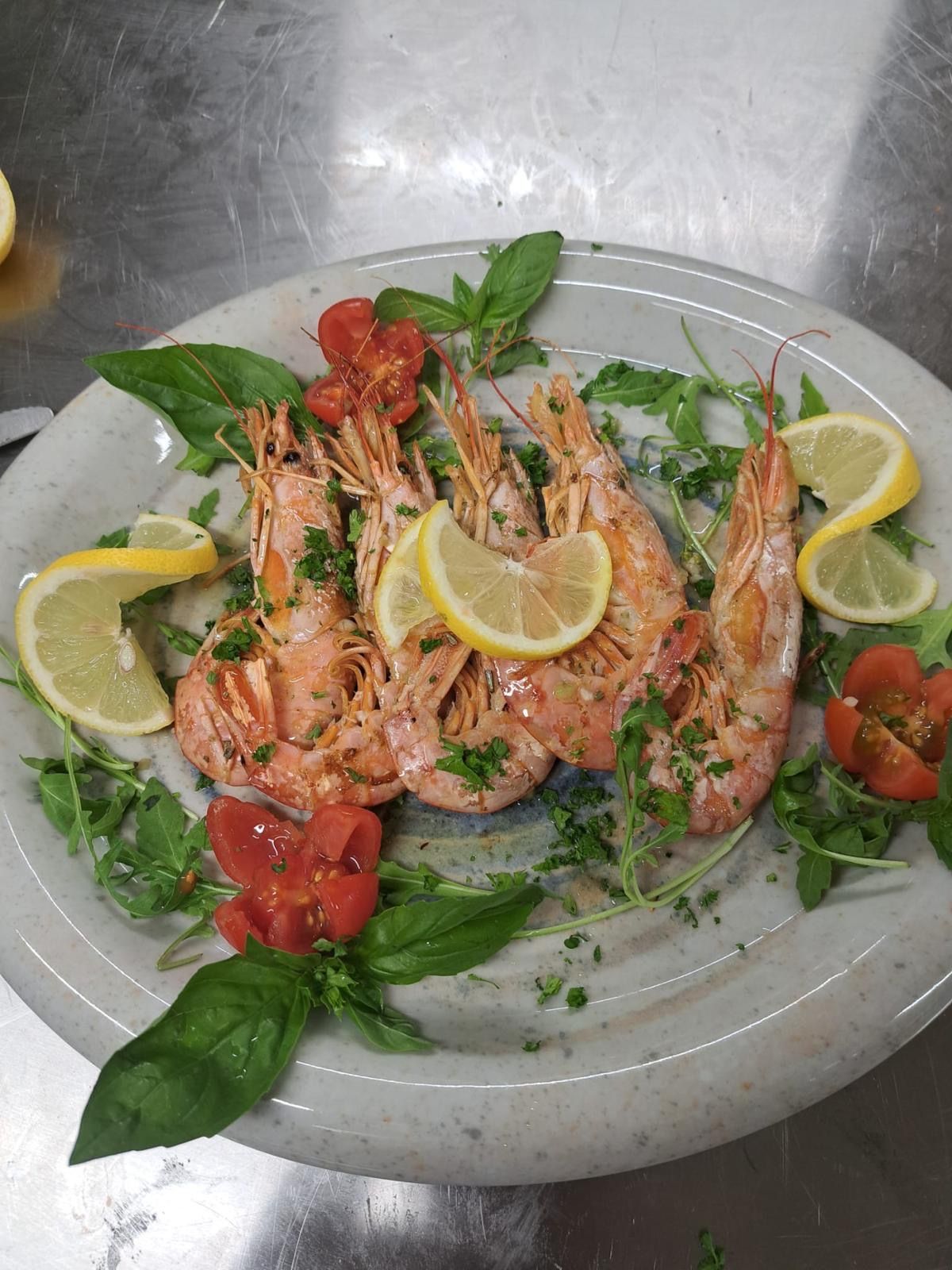 un plat de gambas avec de la roquette, des tranches de citrons et des herbes fraîches
