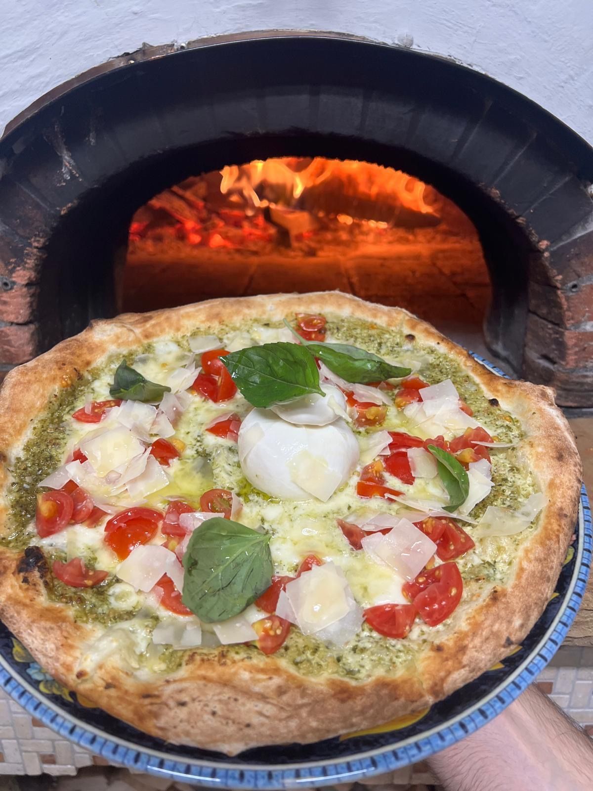 une pizza qui sort du four à bois avec des tomates et une mozzarella dessus.
