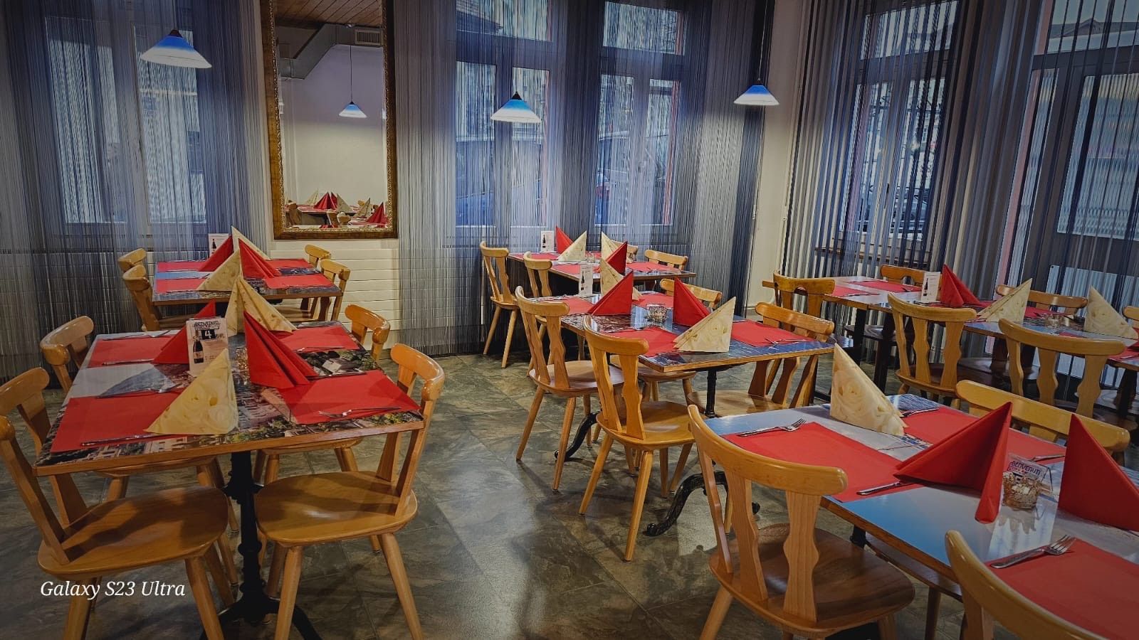 une salle de restaurant avec des tables, chaises et des sets de table rouges