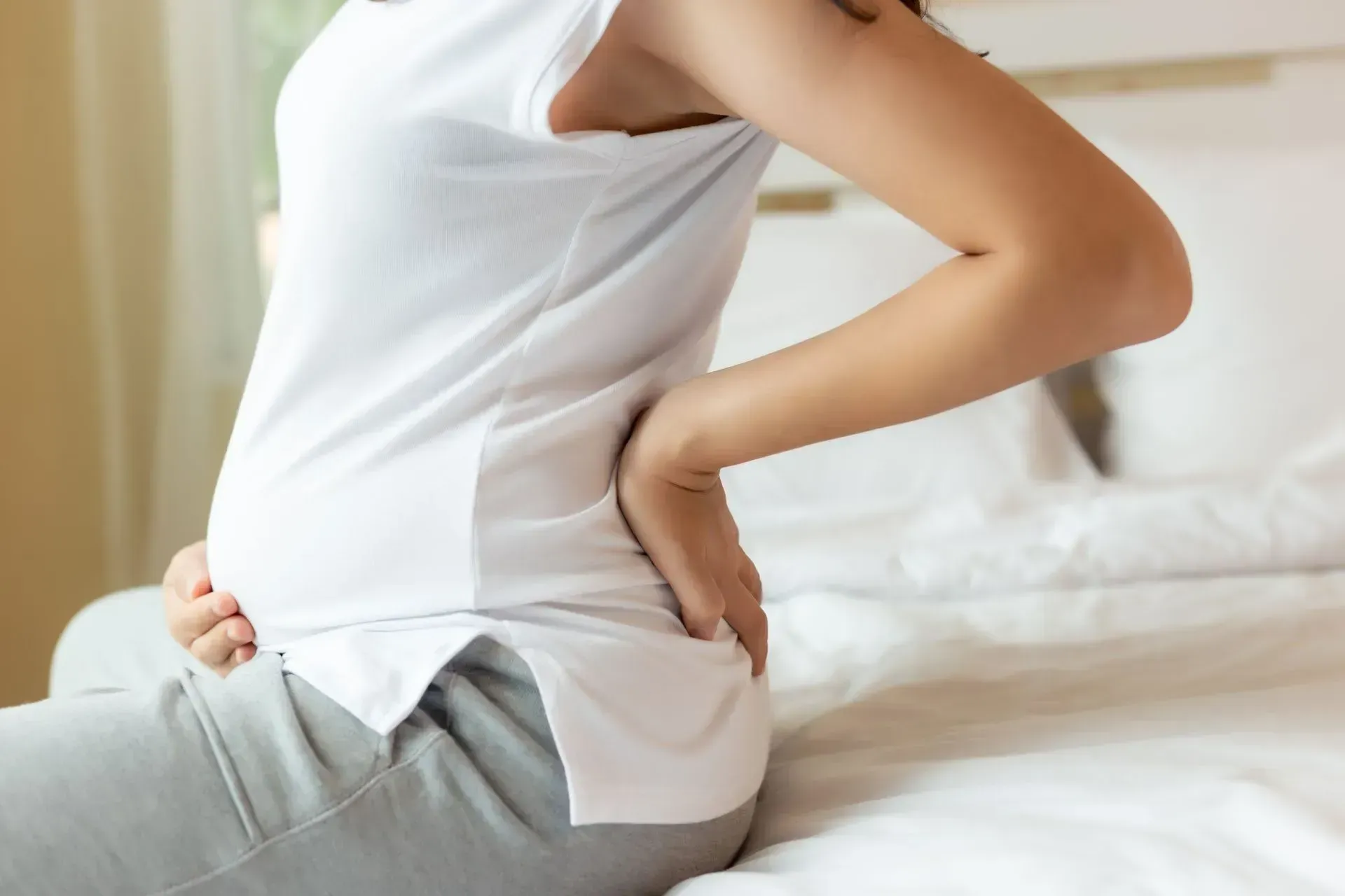 Une femme est assise sur un lit et se tient le dos à cause de la douleur.