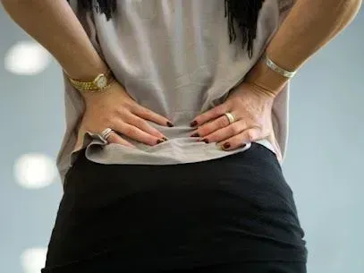 Une femme se retient le dos de douleur.