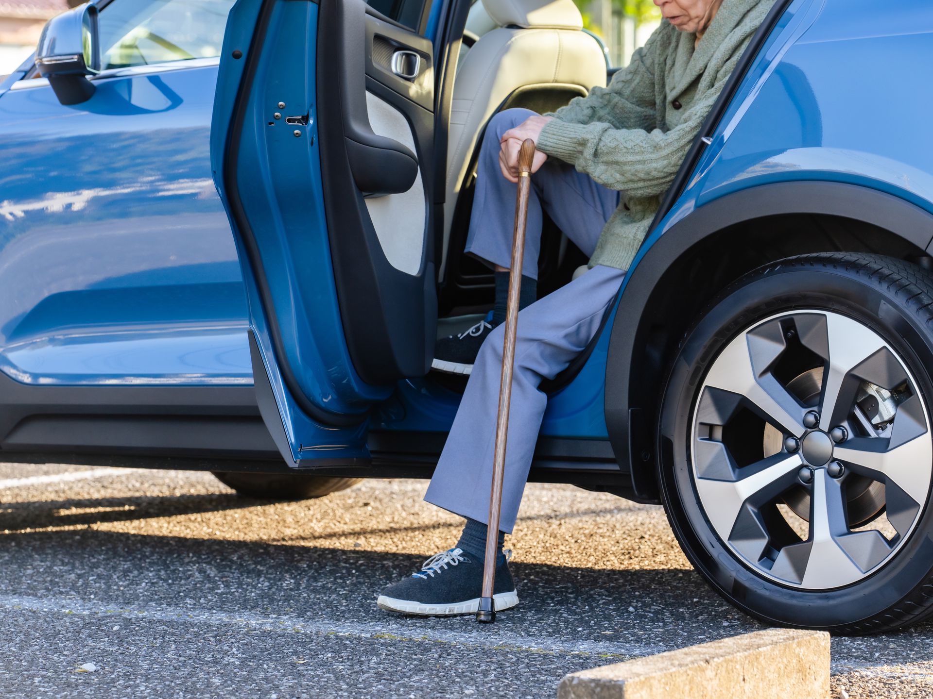 Une personne âgée sort d'une voiture bleue avec une canne dans un parking