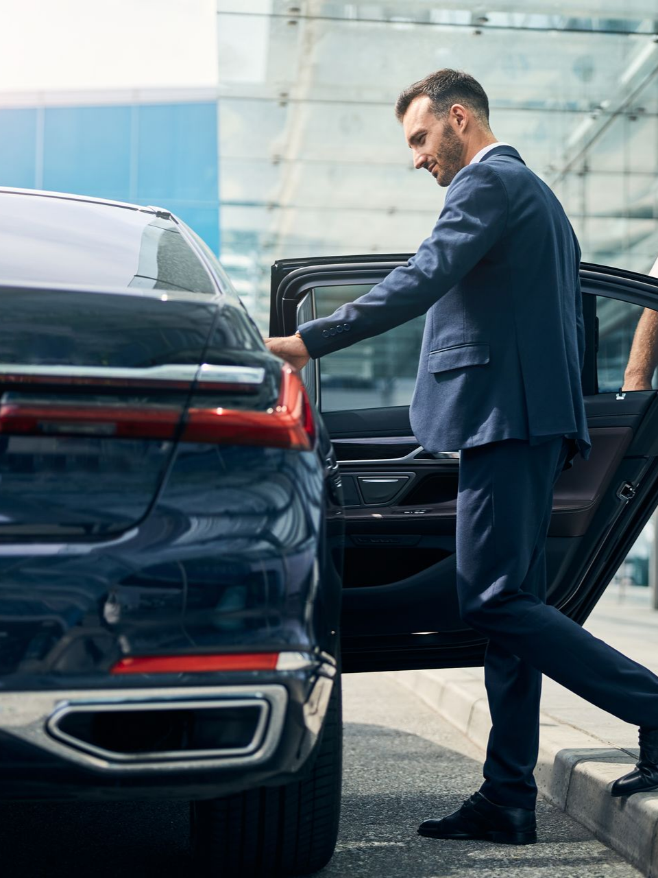 Un homme d'affaires en costume bleu sortant d'une voiture de luxe noire 