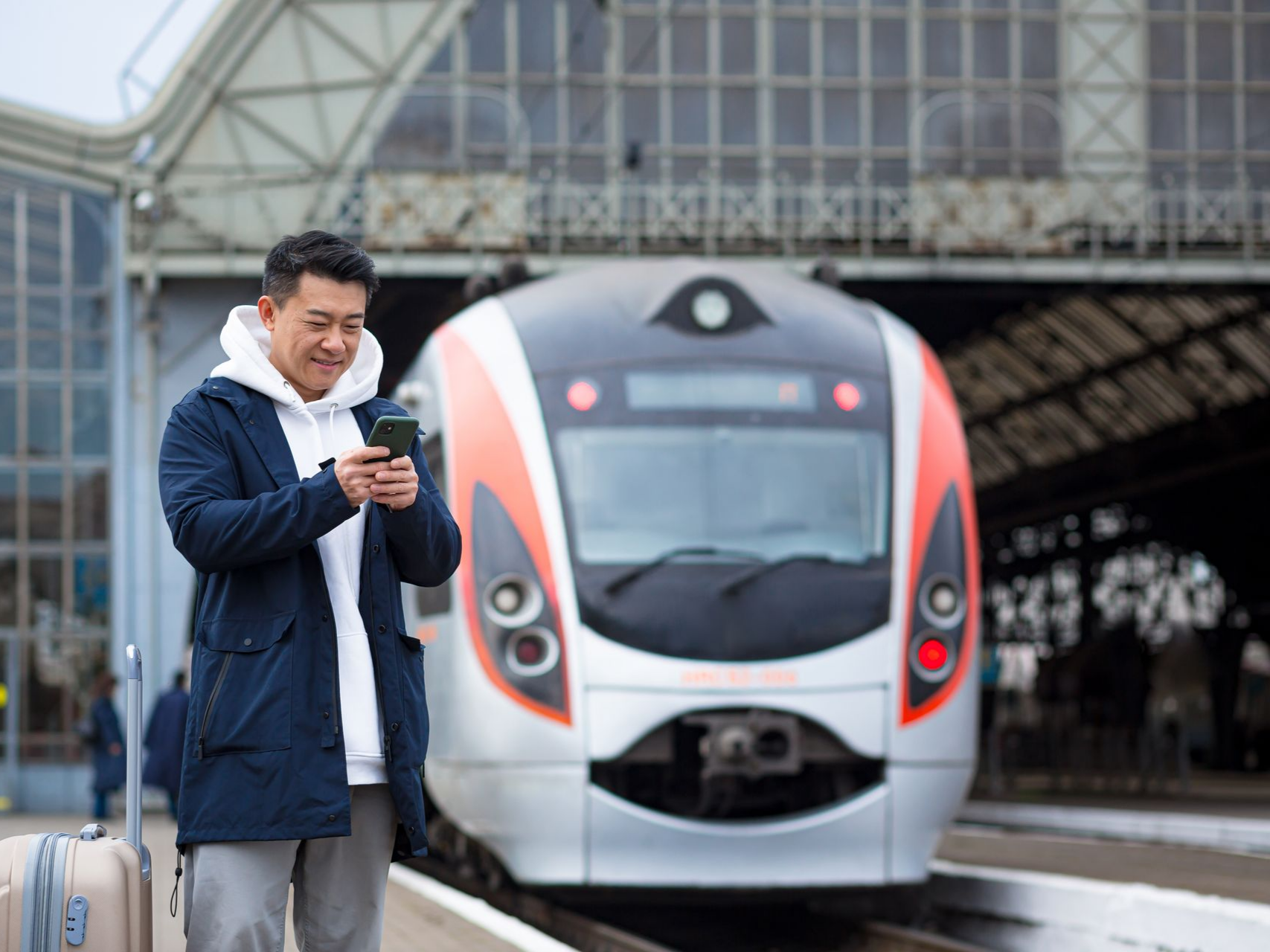 Un homme à la gare regarde son téléphone avec un train en arrière-plan.