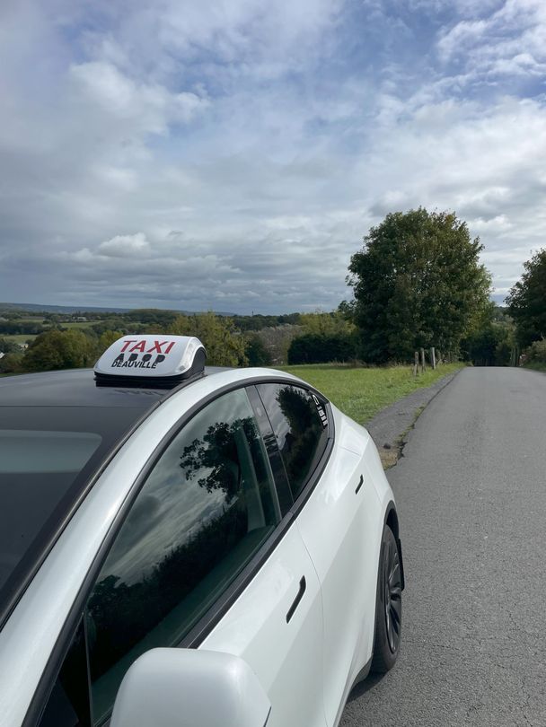 Taxi Tesla blanc garé sur une route avec une vue panoramique sur la campagne