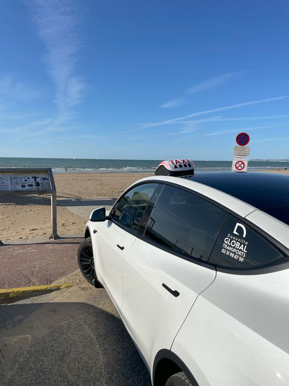 Tesla blanche garée sur une plage ; ciel bleu, océan en arrière-plan