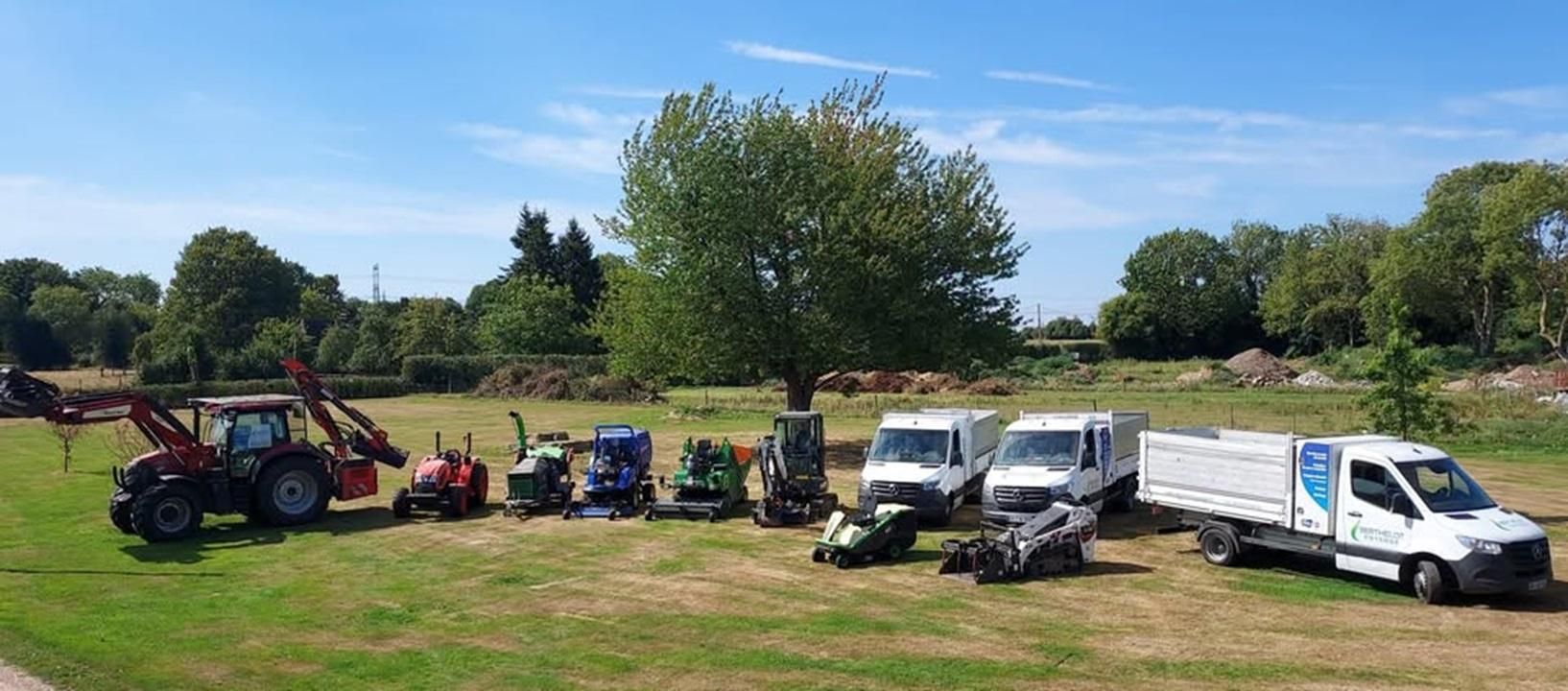 Un groupe de véhicules d'aménagement paysager stationnés sur l'herbe, avec un arbre en arrière-plan.