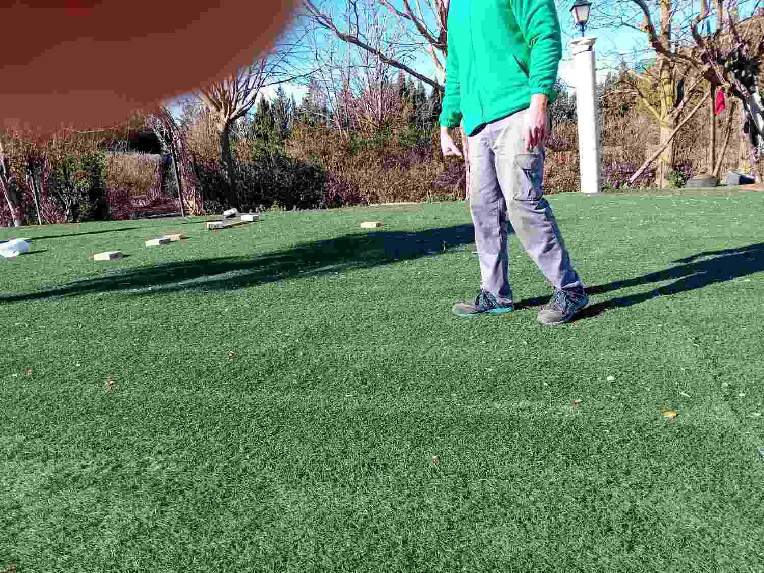 Persona de pie en un campo de hierba al aire libre, vestida con una camisa verde y pantalones grises.