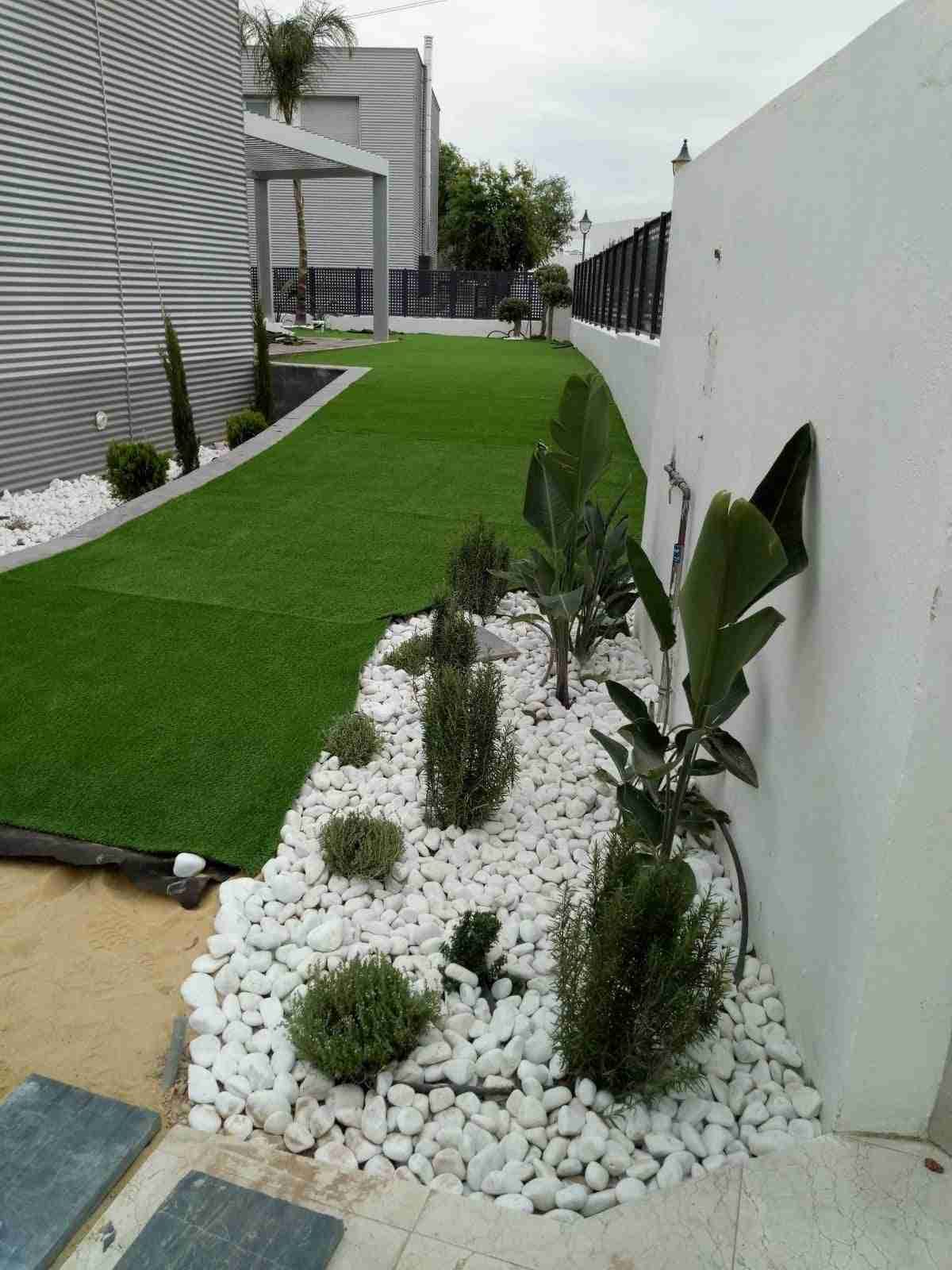 Patio trasero moderno con césped verde, parterre de guijarros blancos y paredes blancas.