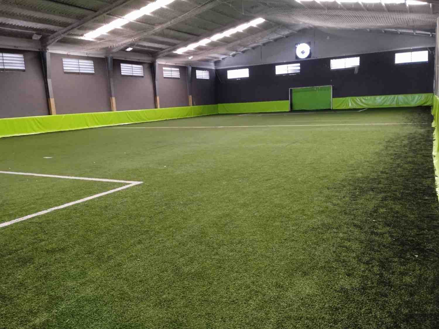 Cancha de fútbol sala con césped artificial, paredes verdes e iluminación cenital.
