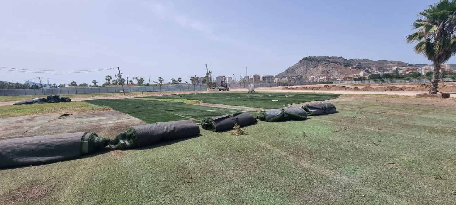 Campo de hierba con varias tuberías negras tendidas, un sendero de tierra y una colina rocosa al fondo.