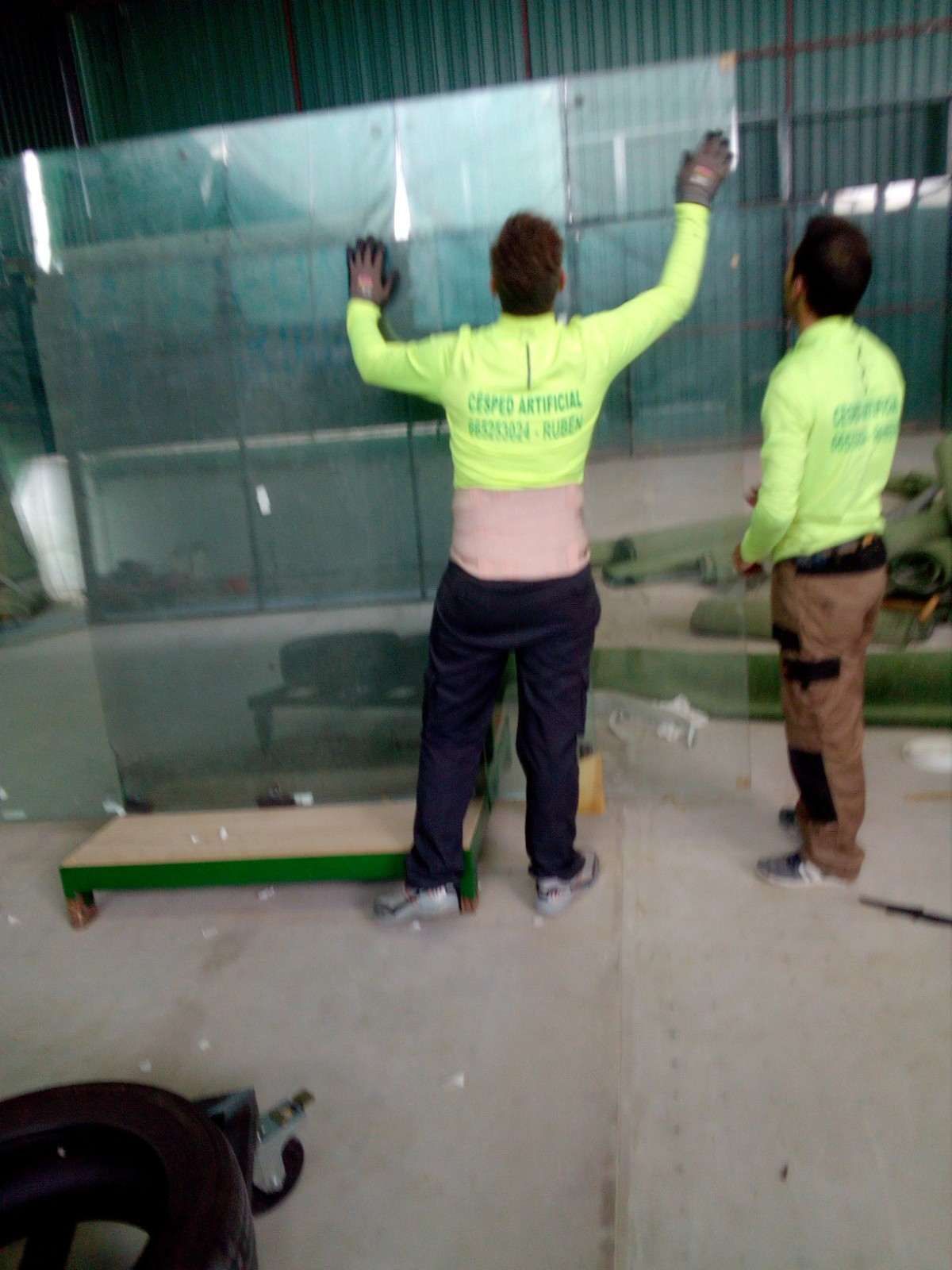 Dos trabajadores con camisetas de neón inspeccionan una pared cubierta de malla verde en una zona de construcción.