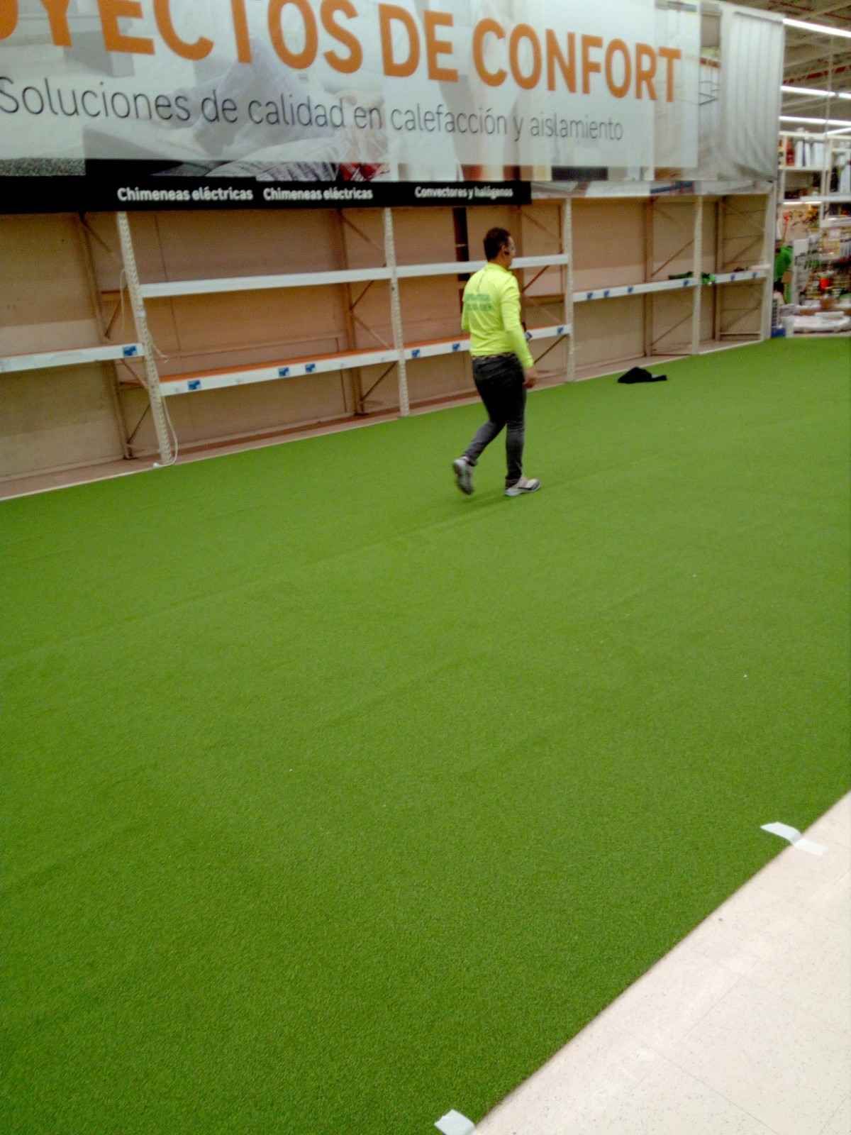 Una persona camina sobre césped artificial de color verde brillante junto a unas estanterías.