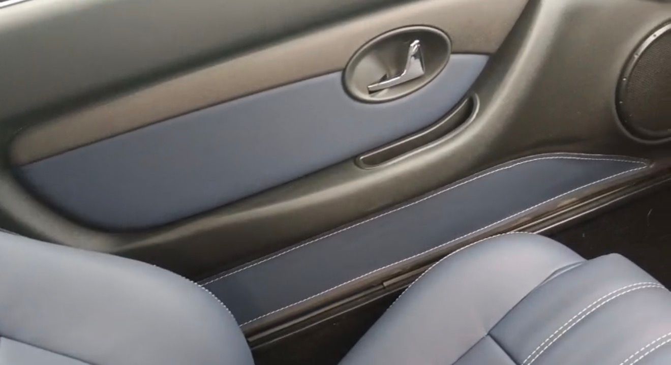Interior de la puerta del coche con tapicería azul y gris, tirador plateado y borde del asiento visible.
