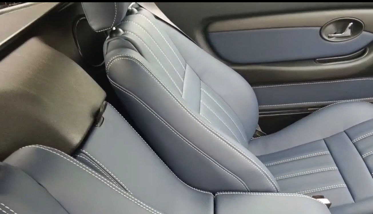 Primer plano de un asiento de coche de cuero gris con costuras blancas y una manija de puerta al fondo.