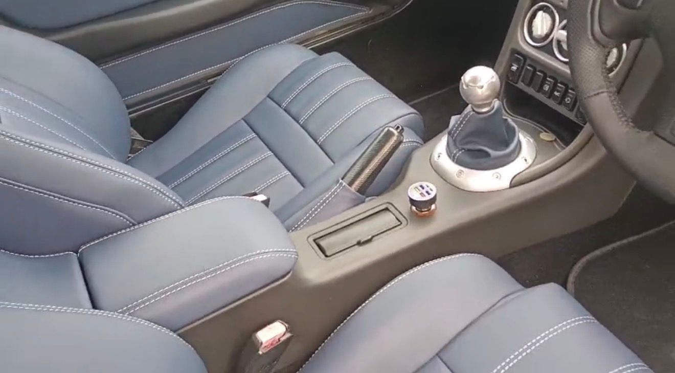 Interior del coche con asientos de cuero azul y palanca de cambios manual entre la consola central y los asientos delanteros.