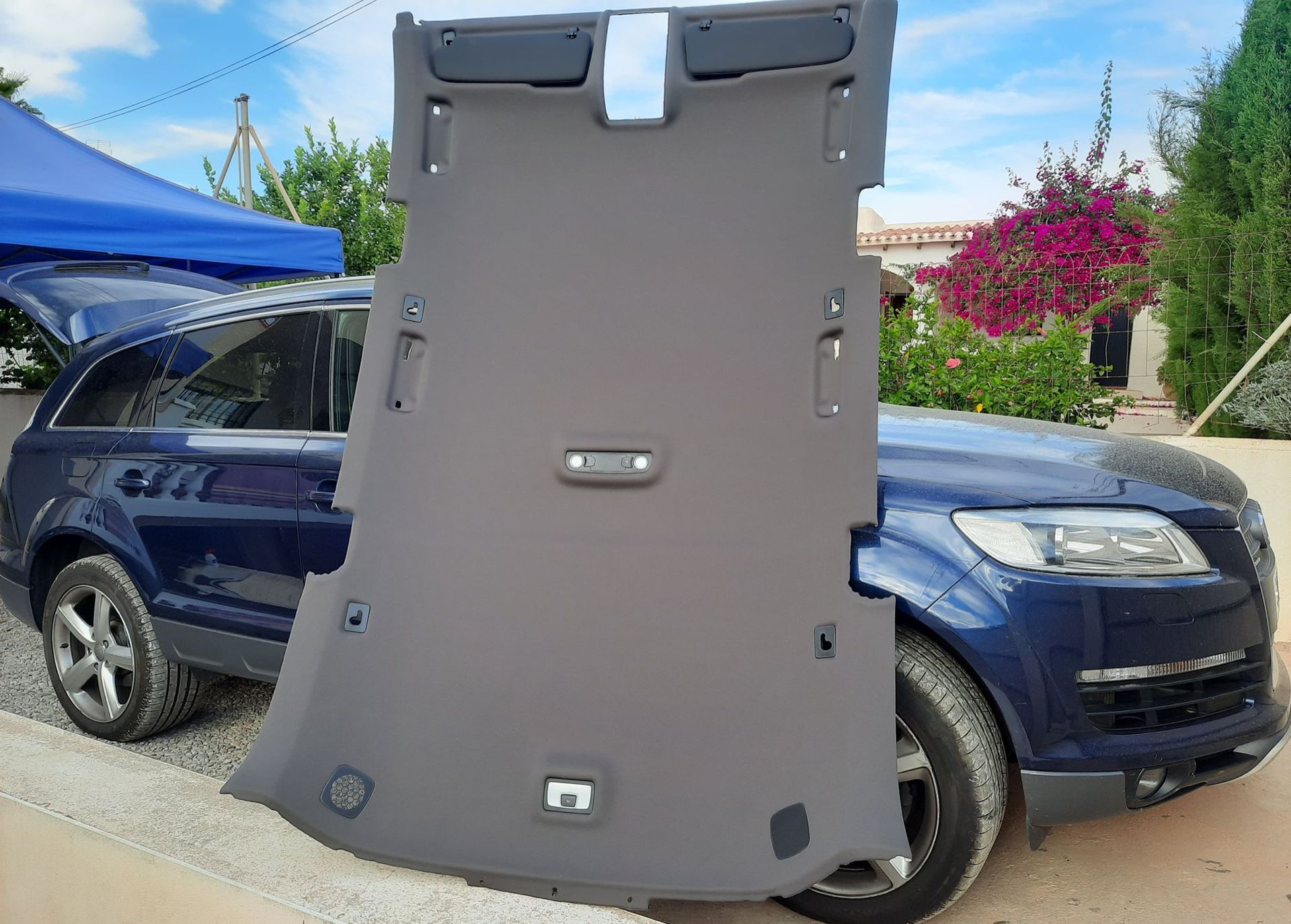 Panel gris de la puerta de un coche, apoyado en posición vertical frente a un SUV azul en el exterior.