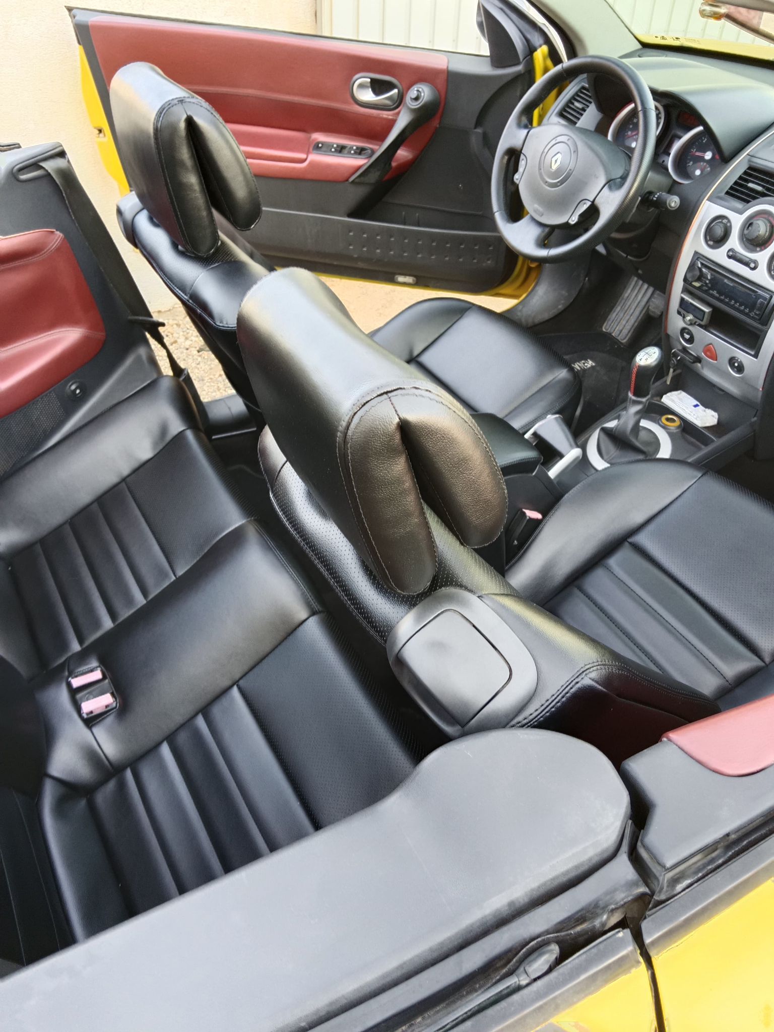 Interior de coche lujoso con asientos, salpicadero y volante de cuero negro y rojo.