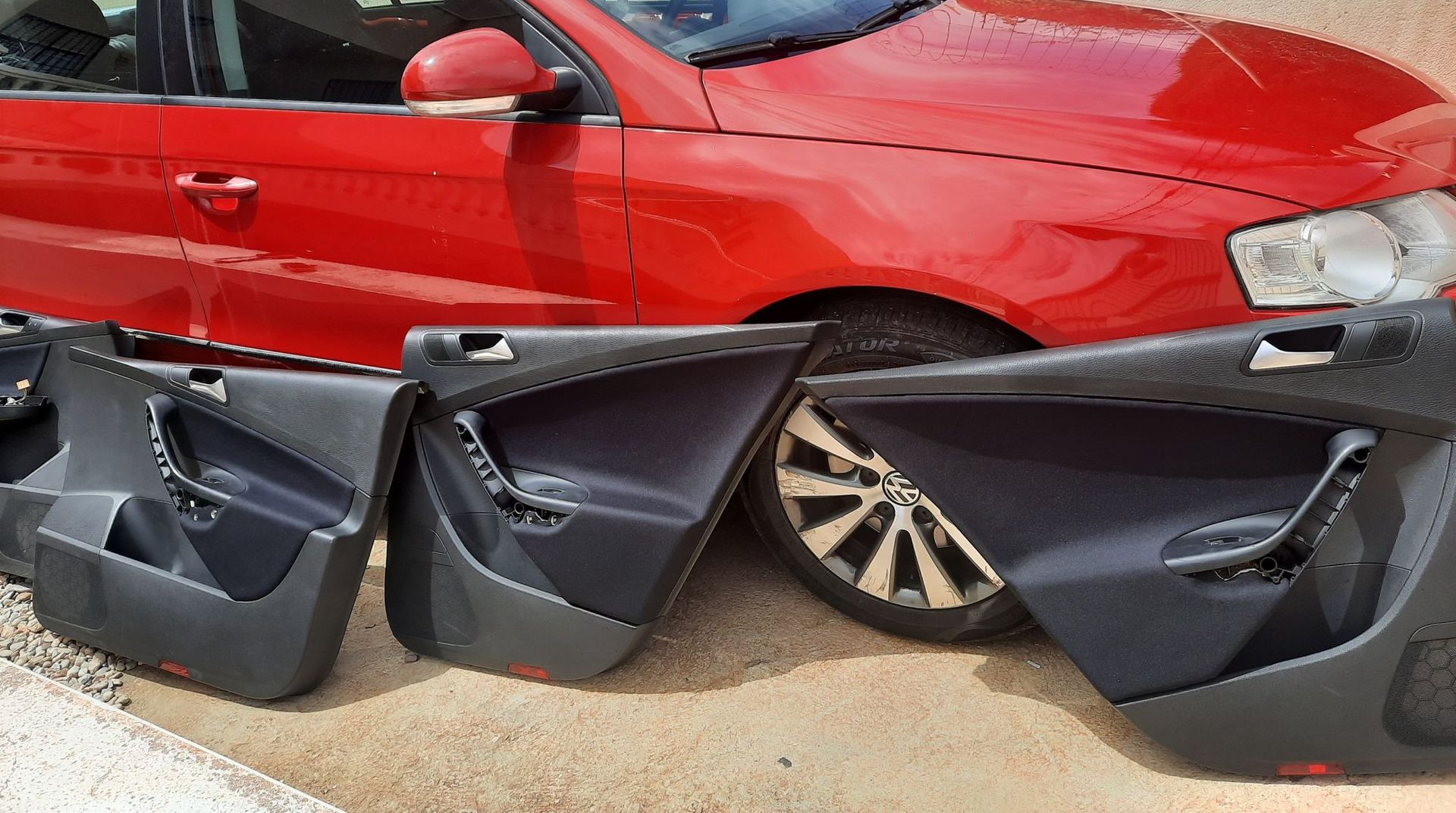 Coche rojo con varios paneles de puerta negros sueltos alineados delante.