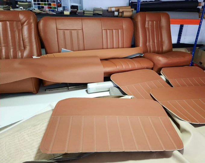 Cojines y respaldos de asientos de coche de cuero marrón dispuestos sobre una mesa de trabajo en un taller.