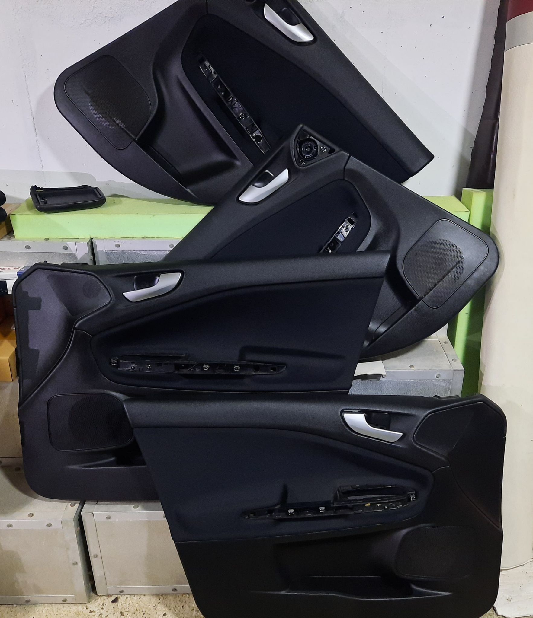 Asientos y paneles de puertas de coche negros apilados en un taller o área de almacenamiento.