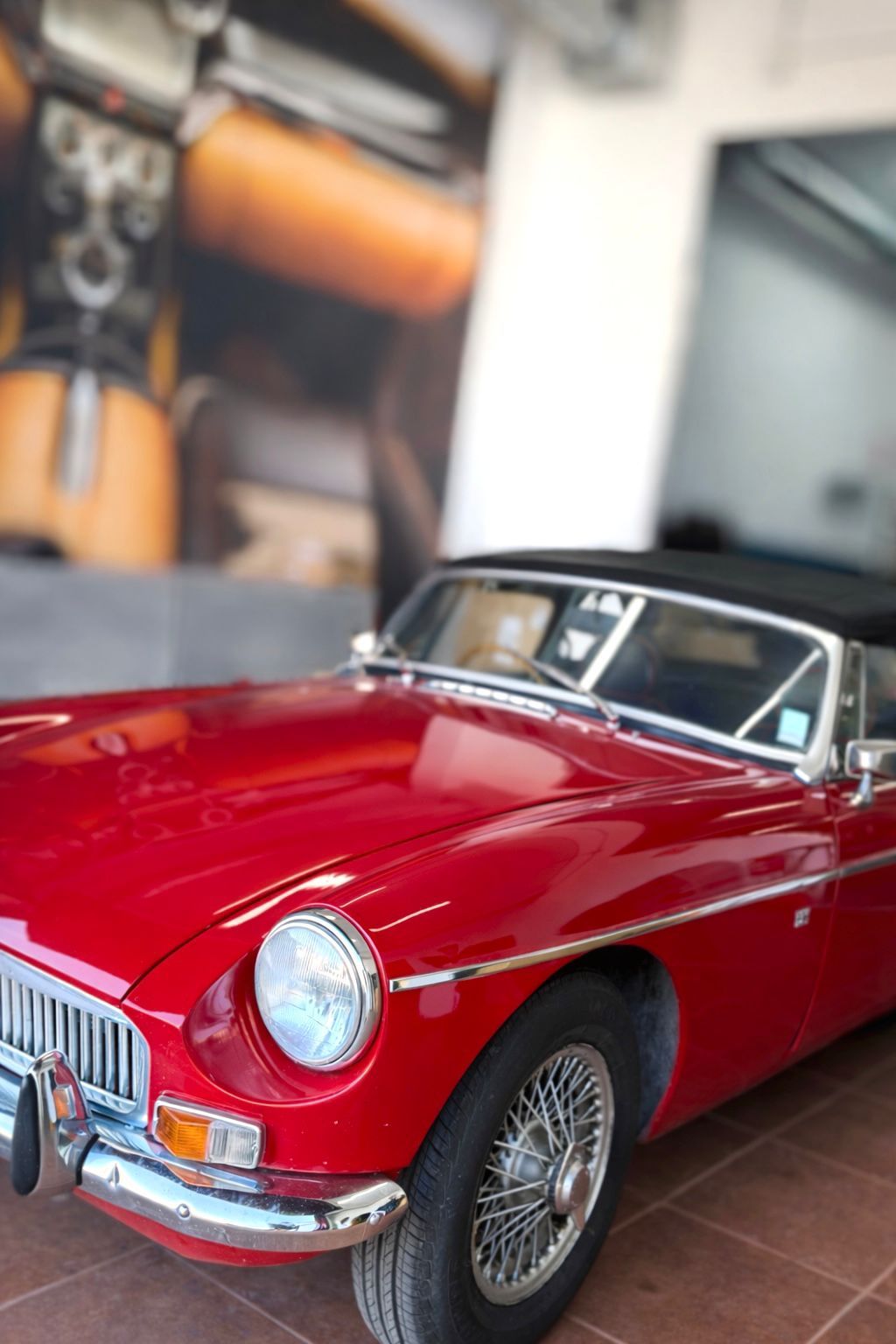 Coche deportivo descapotable rojo clásico aparcado en el interior sobre suelo de baldosas.