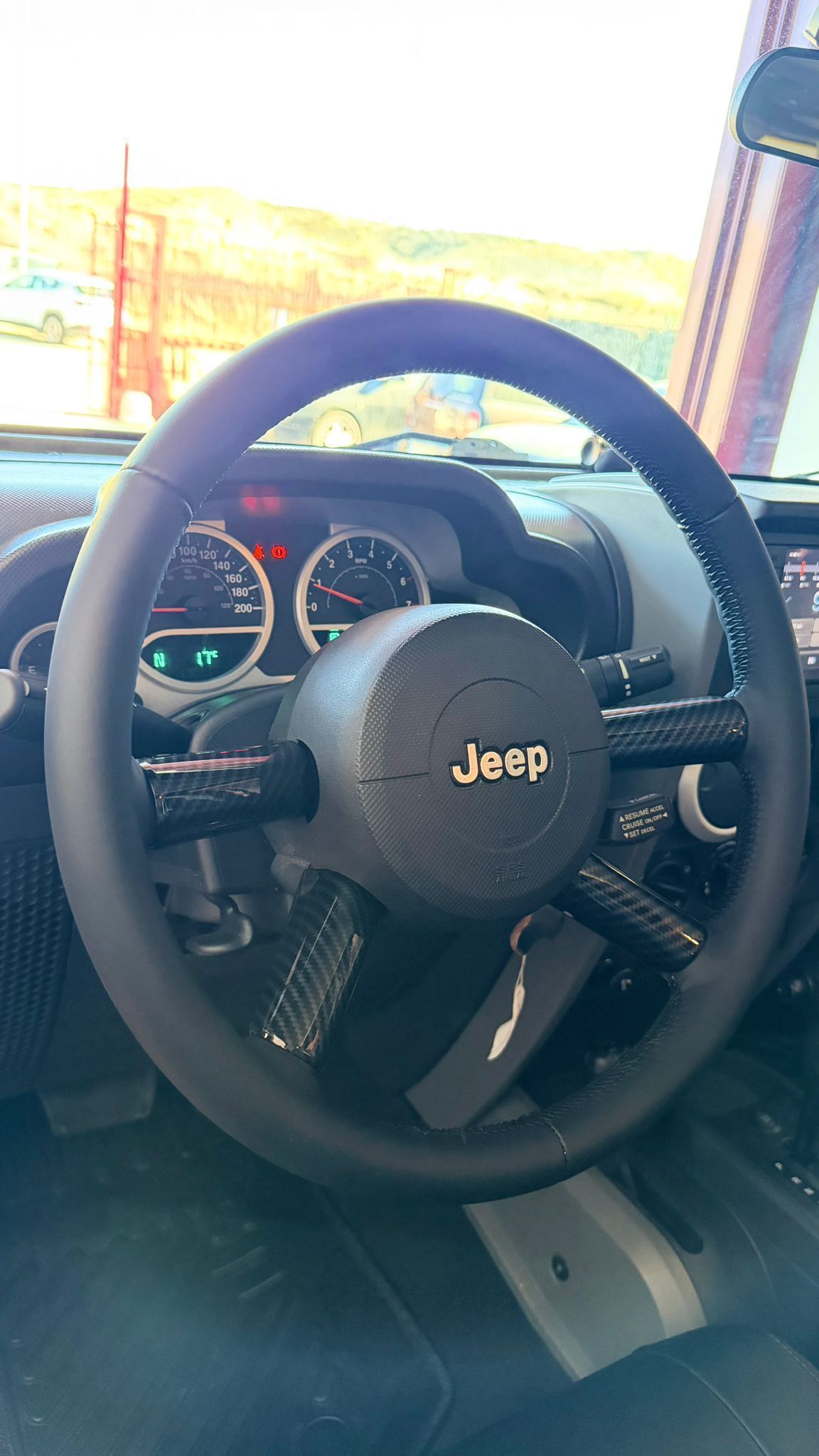 Interior del volante y del tablero del Jeep, con los indicadores iluminados y la luz del sol entrando por el parabrisas.