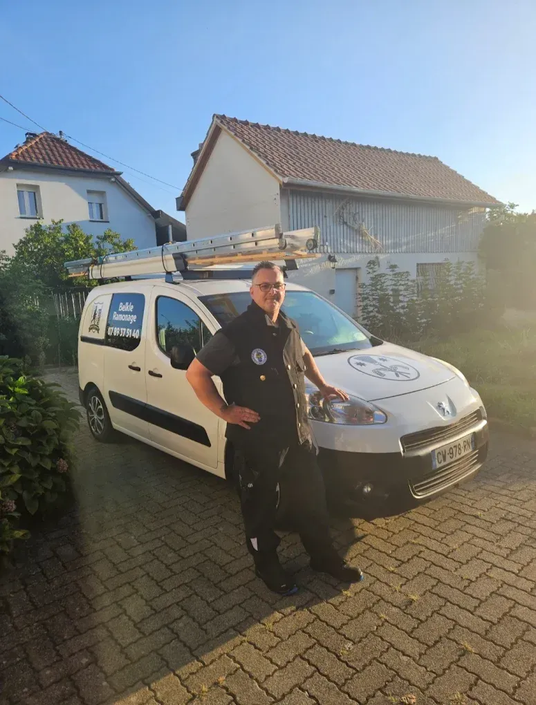 Un professionnel souriant, à côté d'une camionnette blanche équipée d'un porte-échelle.
