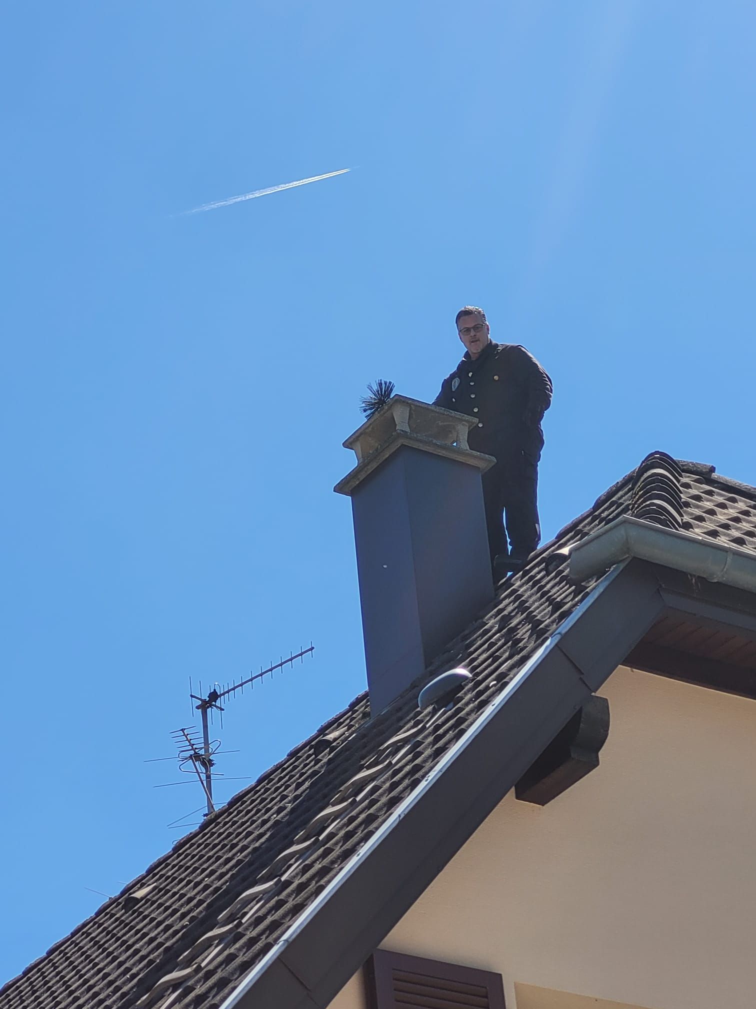 Gros plan d'une solin de cheminée métallique installée sur un toit en bardeaux, avec une maison floue en arrière-plan.
