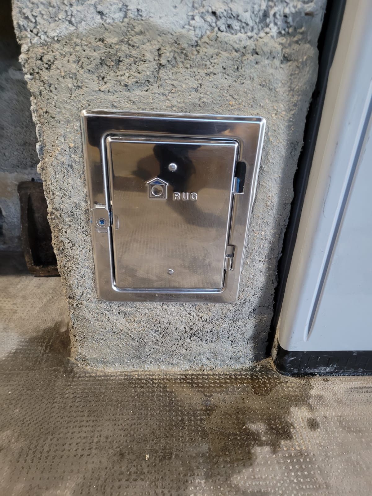 Boîtier métallique encastré dans un mur en béton, à côté d'un seuil de porte.