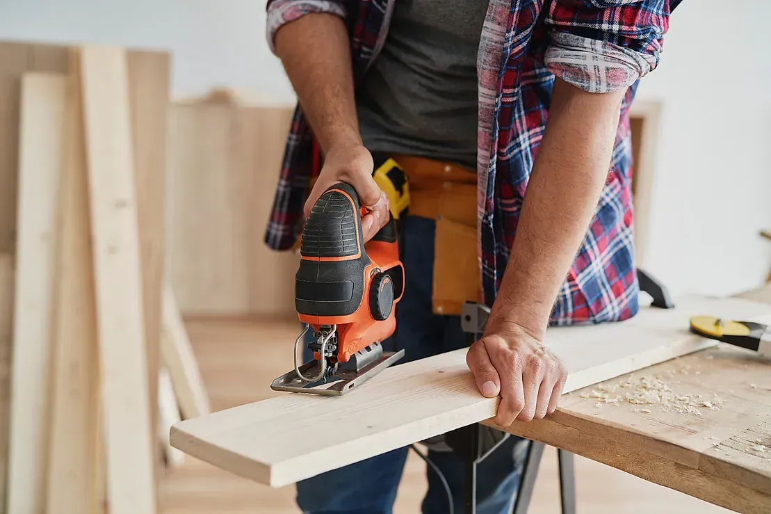 Un hombre está usando una sierra caladora para cortar un trozo de madera.