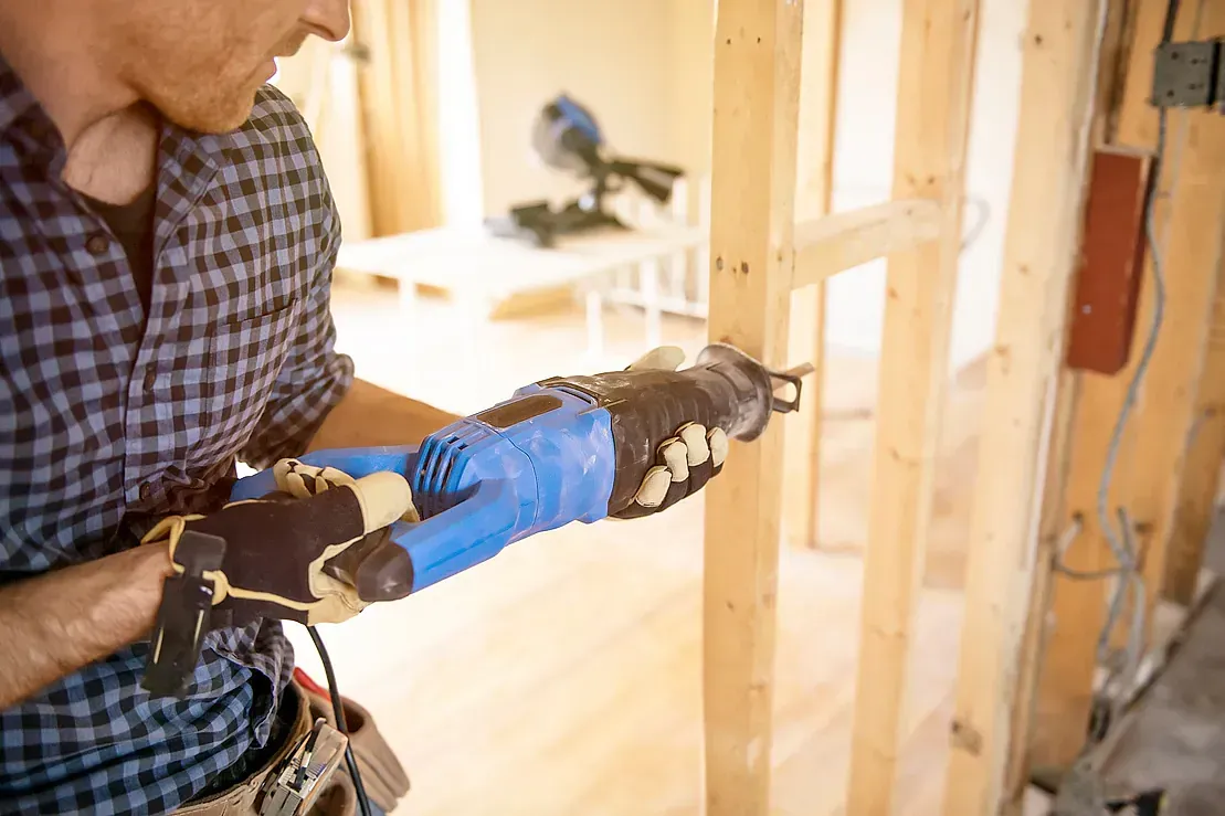 Un hombre está usando una sierra para cortar un agujero en una pared de madera.
