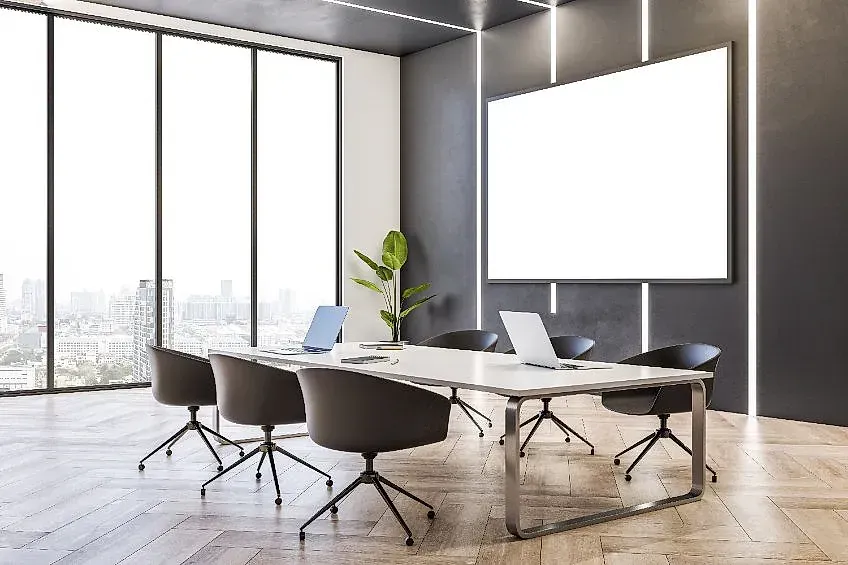 Una sala de conferencias con una mesa, sillas, computadoras portátiles y una pantalla de proyector.