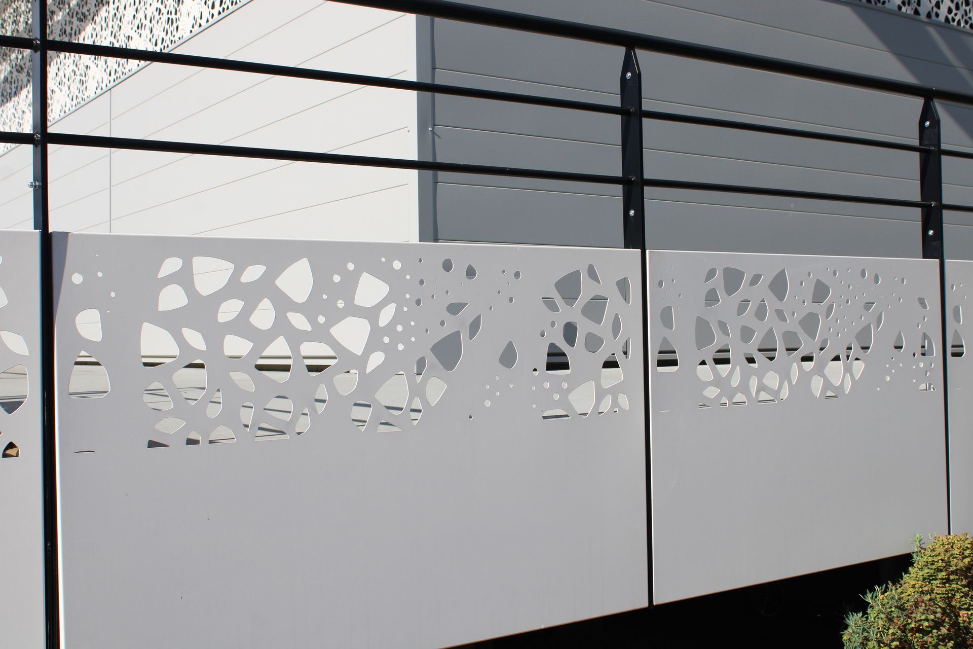 Panneaux de balcon en métal blanc ornés de motifs organiques découpés au laser en forme de branches, montés sur une rambarde noire.