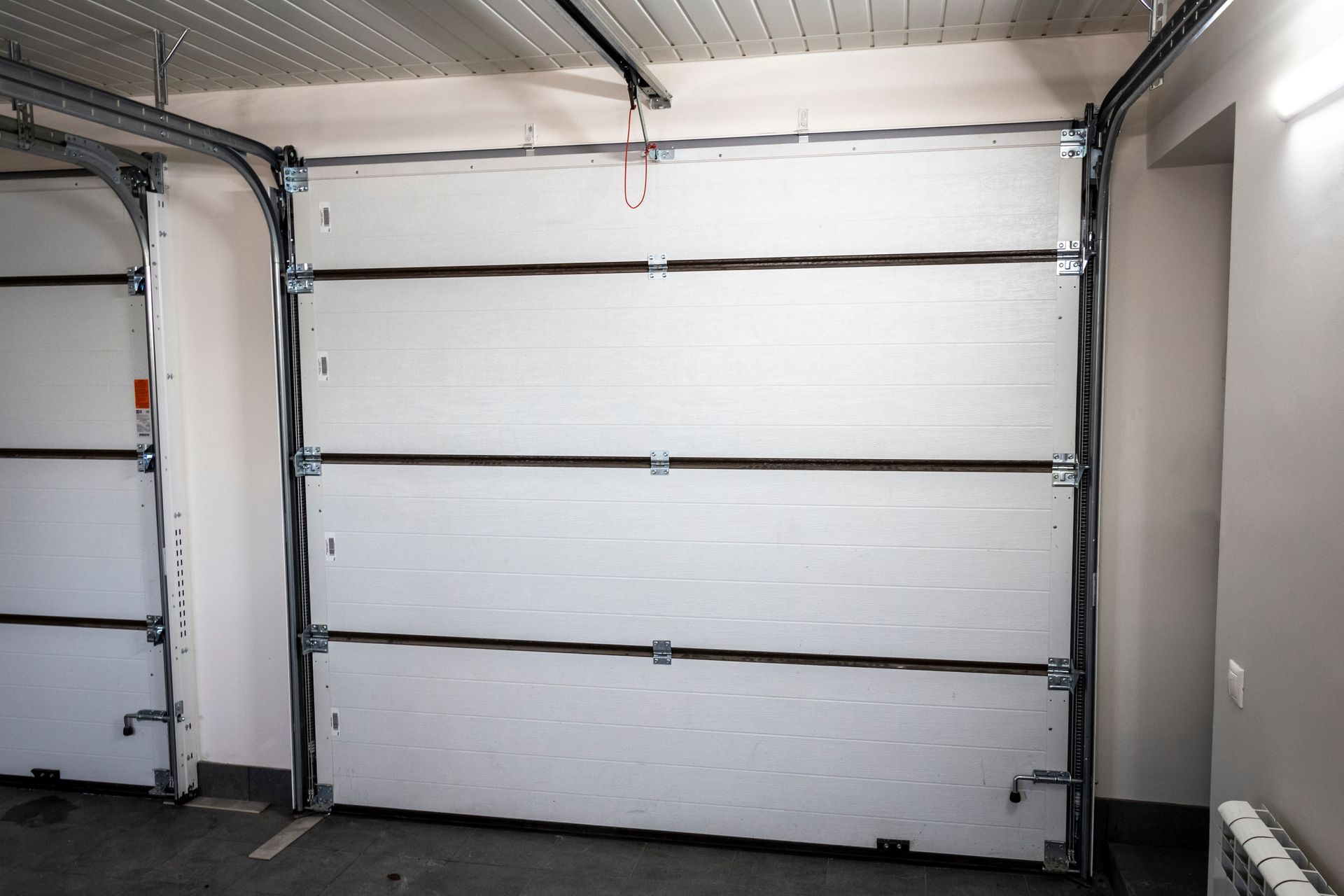 Porte de garage sectionnelle blanche à l'intérieur d'un garage, composée de panneaux horizontaux et de rails métalliques.