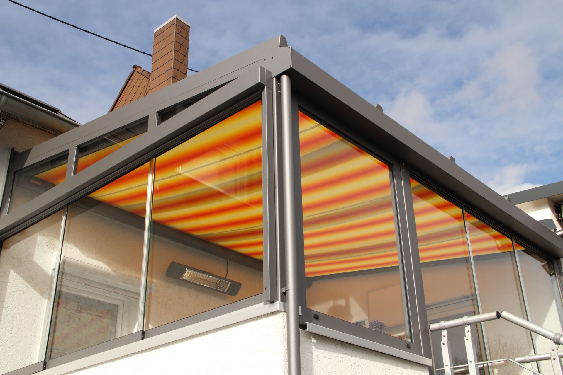 Une terrasse vitrée avec un store rayé orange et jaune rétracté et un chauffage mural.