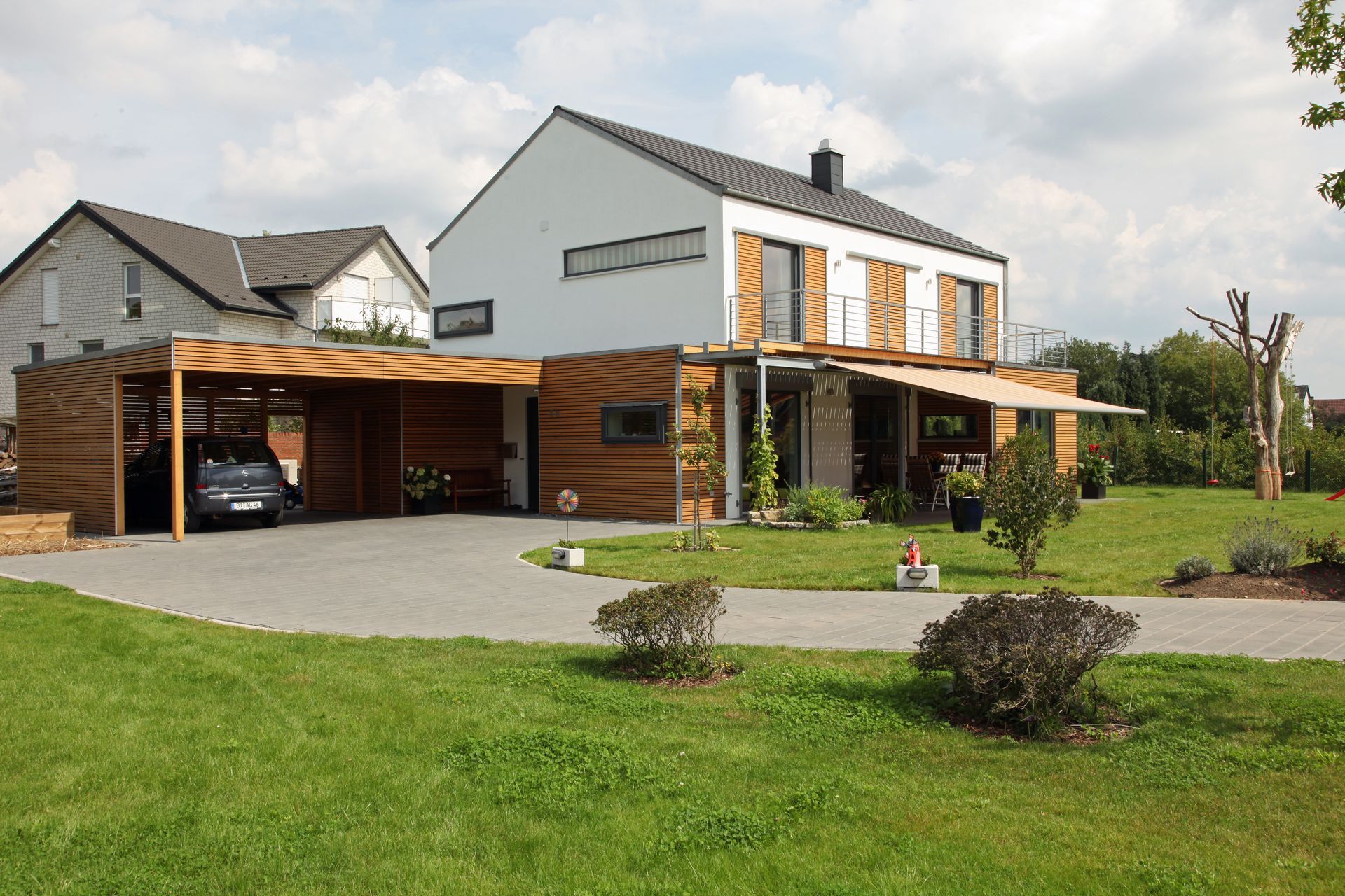 Maison moderne de deux étages, blanche et lambrissée, avec un abri voiture attenant, une allée en gravier et une cour avant gazonnée.