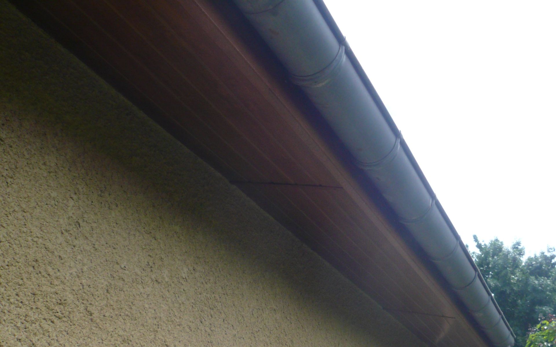 Gros plan sur une gouttière métallique fixée à l'avant-toit en bois d'une maison de couleur beige avec un revêtement en stuc texturé.