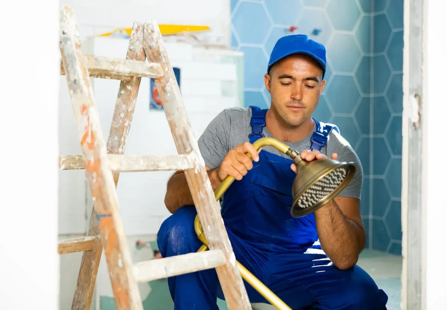 Trabajador con uniforme azul utilizando una lámpara de mano cerca de una escalera en una habitación con azulejos.