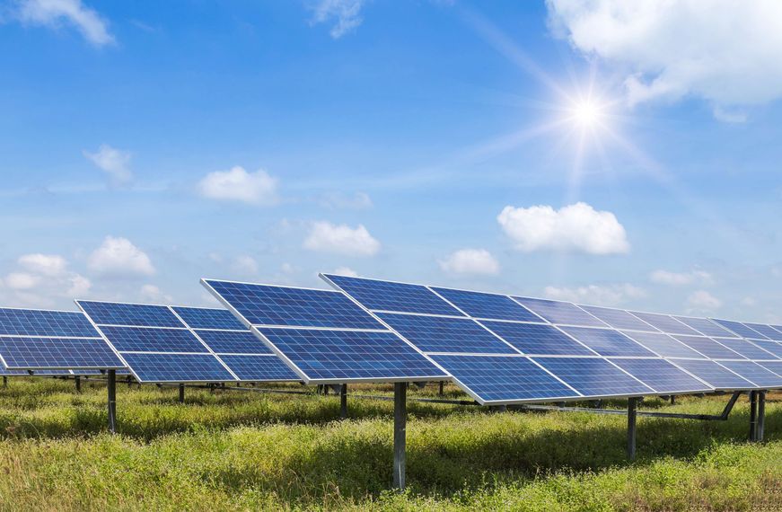 Des panneaux solaires dans un champ herbeux sous un ciel bleu éclatant, entre soleil et nuages.