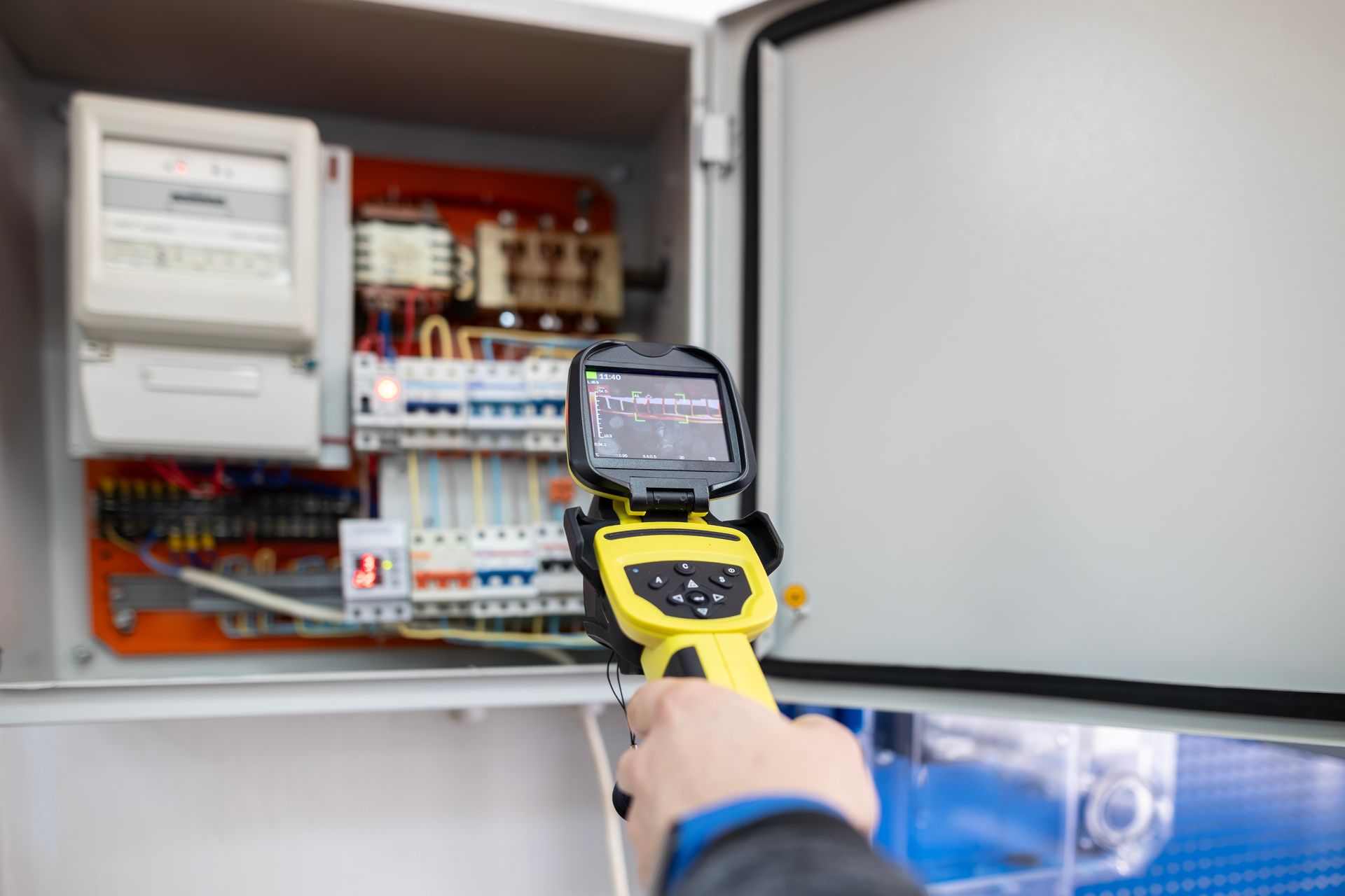 Un technicien utilise une caméra thermique jaune pour inspecter un panneau électrique ouvert.