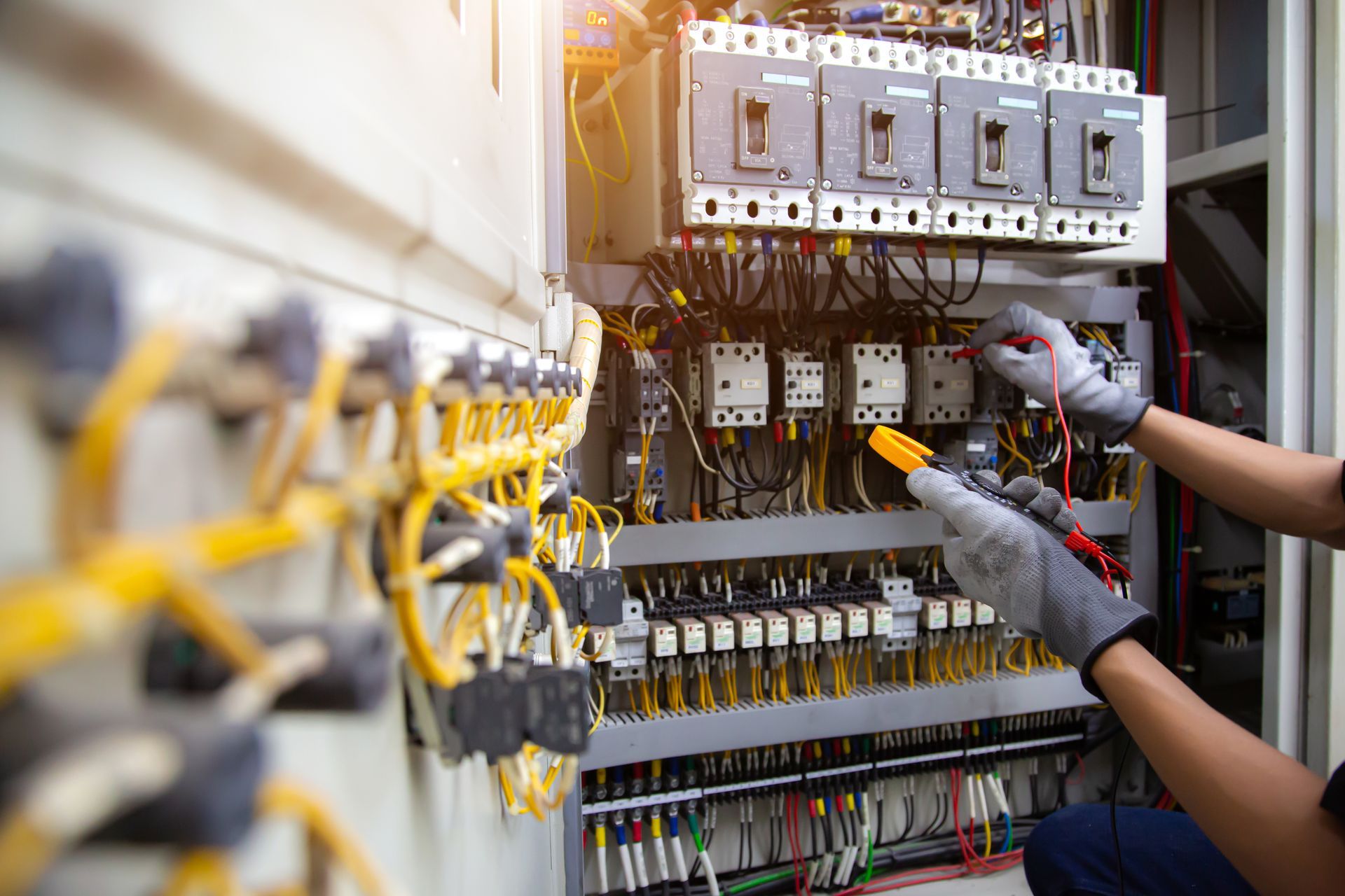 Technicien travaillant à l'intérieur d'un tableau électrique avec des câbles, des disjoncteurs et des outils de test