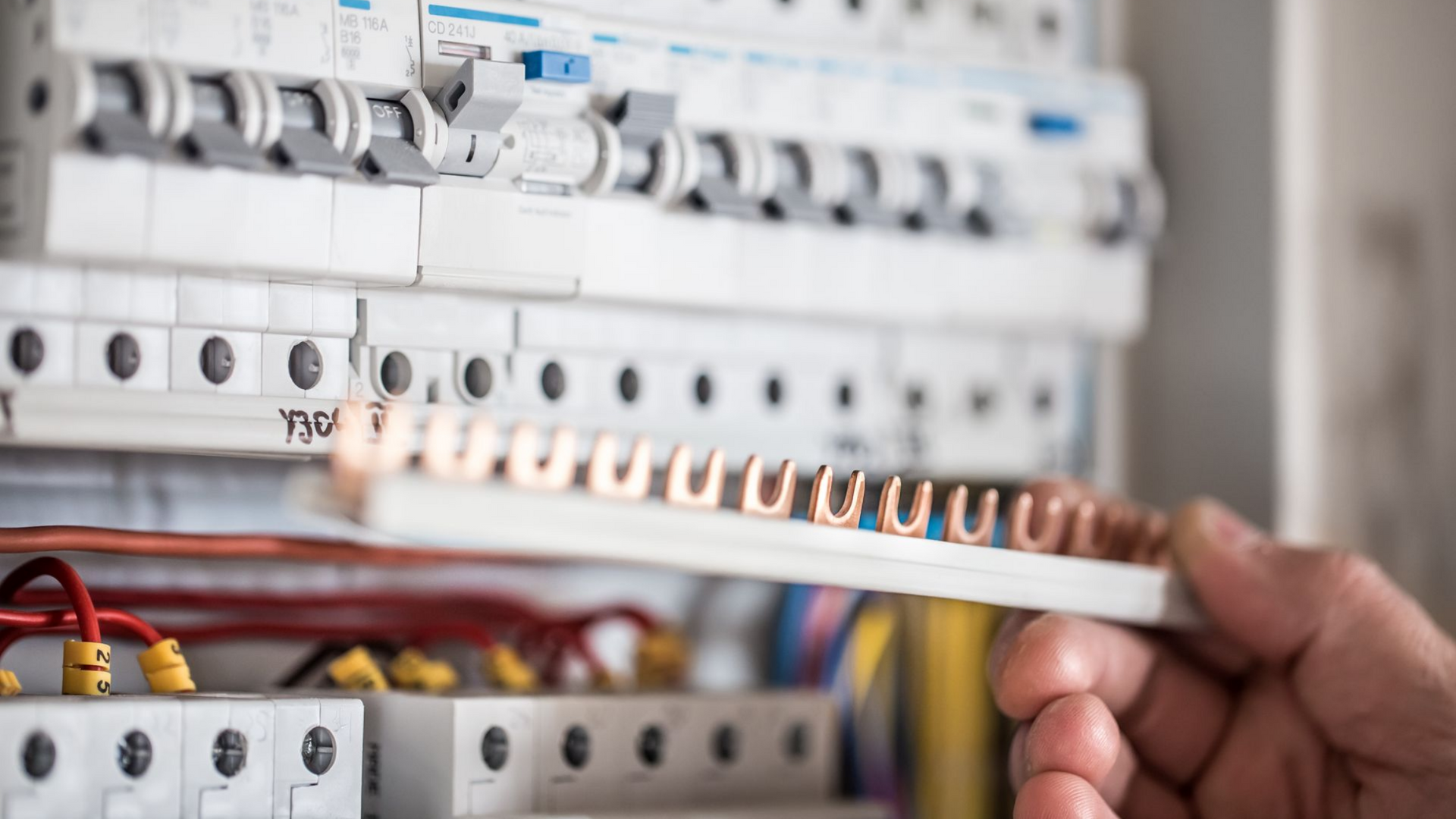 Installation manuelle d'un câble blanc dans un tableau électrique avec disjoncteurs et câblage
